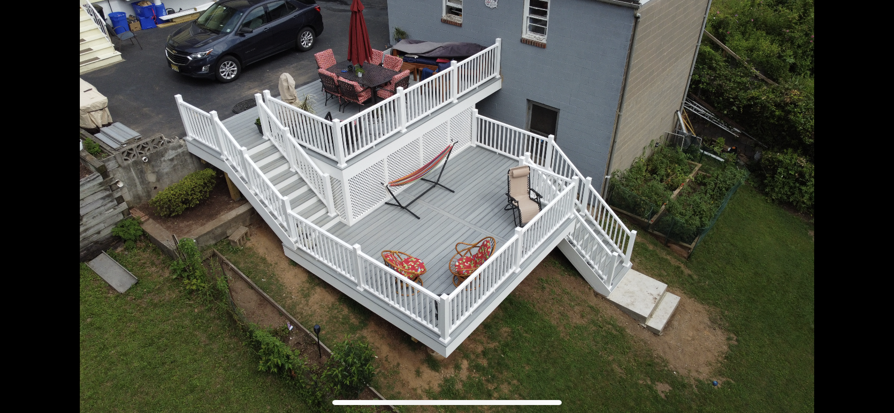 An aerial view of a multi-level white deck attached to a gray house, with seating and a hammock.