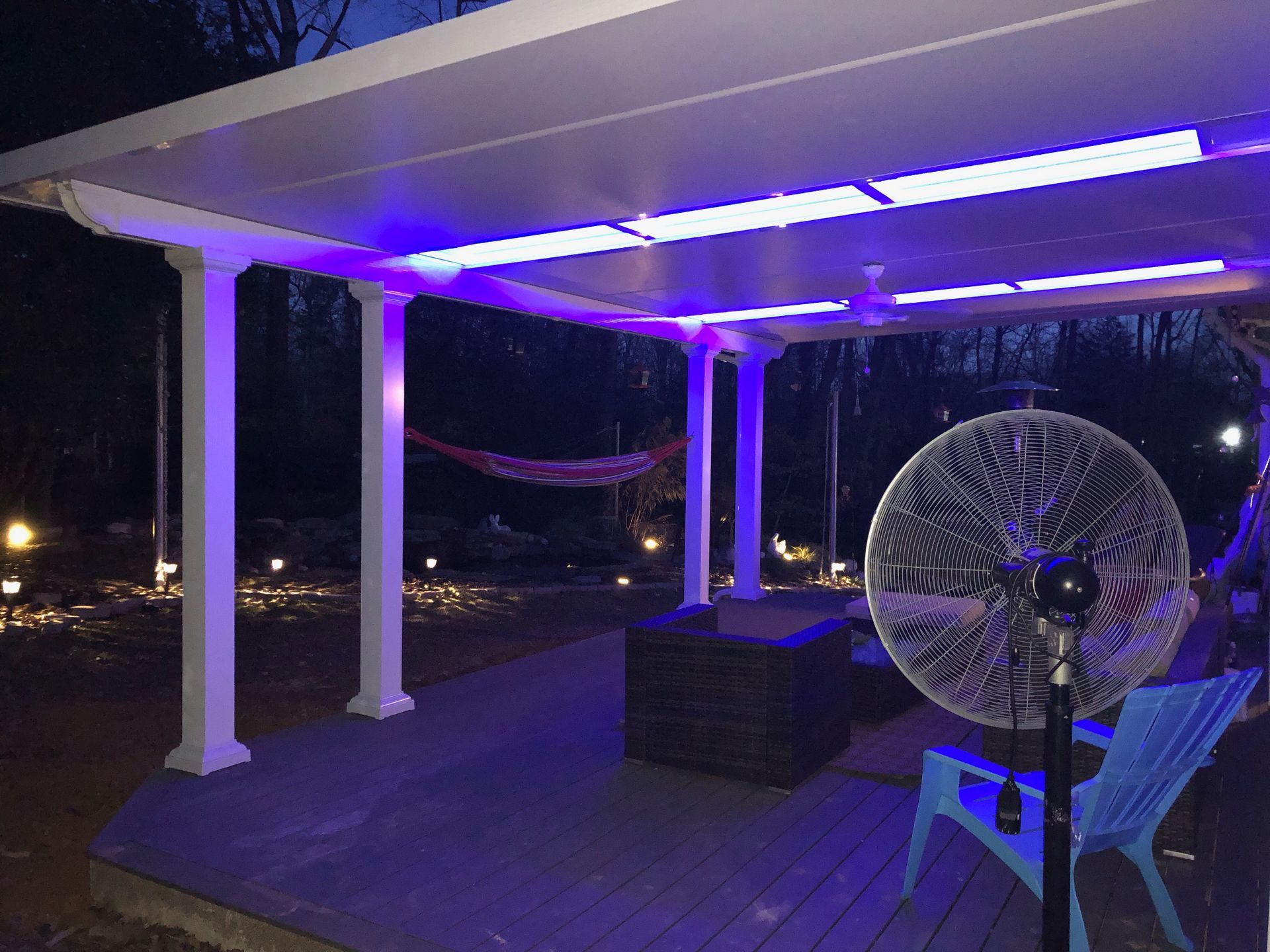 Outdoor patio at night with purple overhead lights and a fan. A hammock hangs in the background.