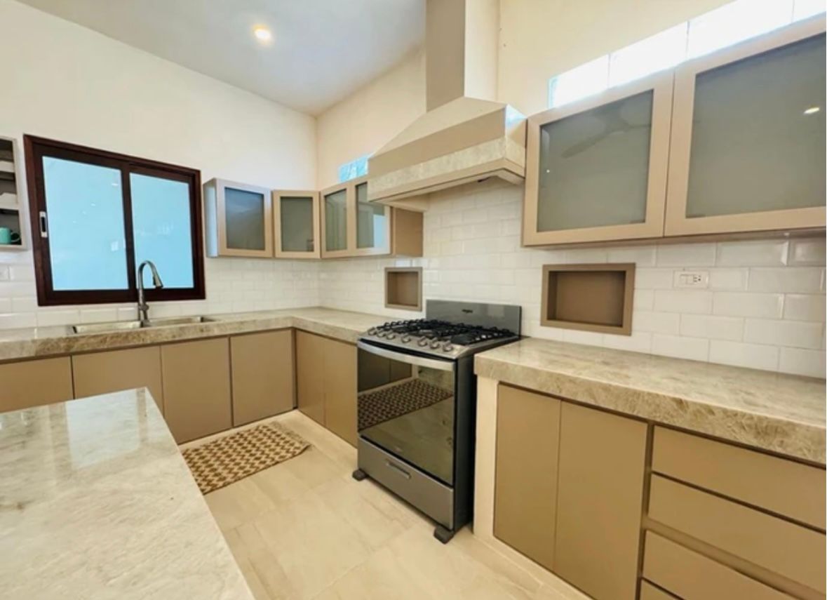 Modern kitchen with tan cabinets, countertops, and stainless steel appliances.