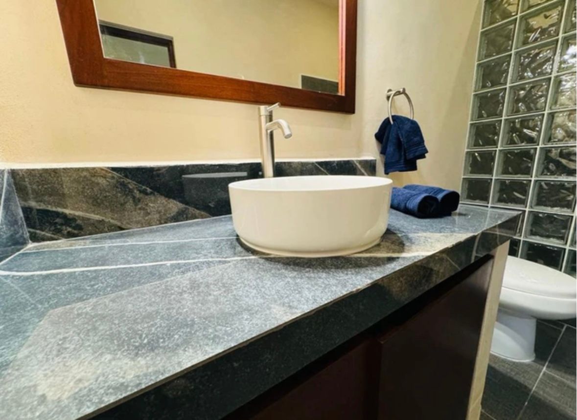 Bathroom with a white bowl sink on a dark countertop. A mirror, towel, and toilet are also visible.