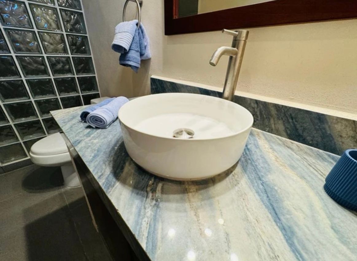 White sink on blue marbled countertop in a bathroom. Faucet, towels, and toilet visible.