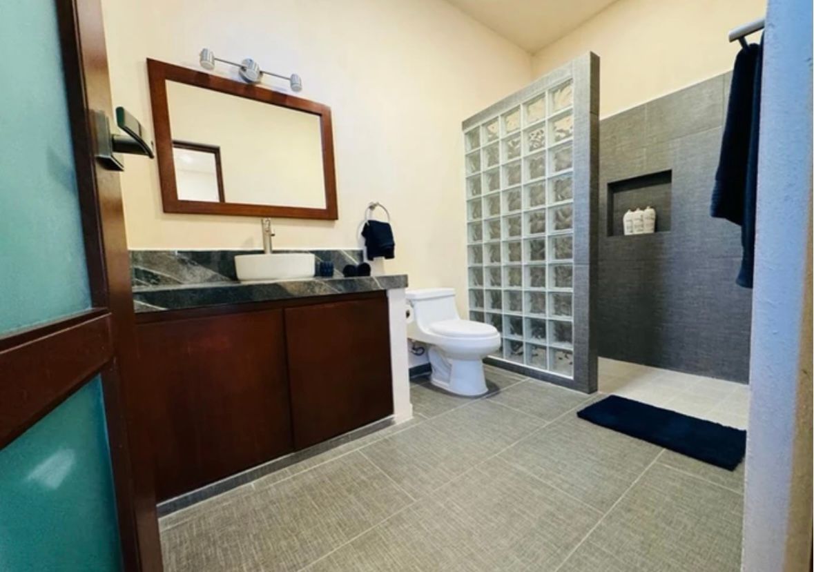 Bathroom with dark wood vanity, white toilet, glass block shower, gray tile floor, and a large mirror.