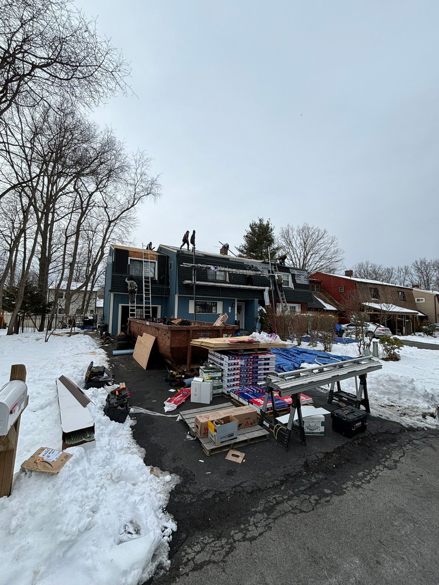 House damaged by fire, debris in front, snow on the ground, overcast sky.