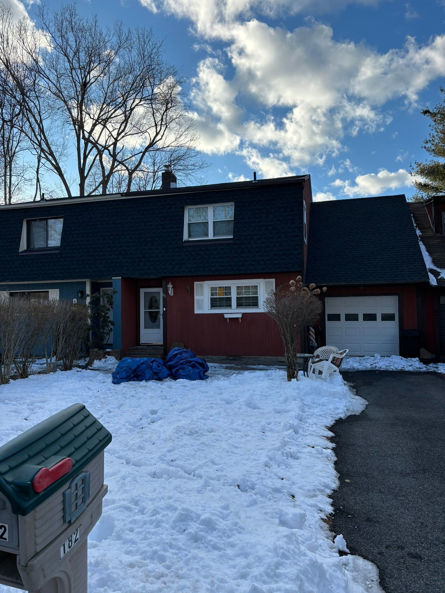Snow-covered row of houses; red facade with white trim; blue bags on the lawn; white garage door; mailbox in foreground.
