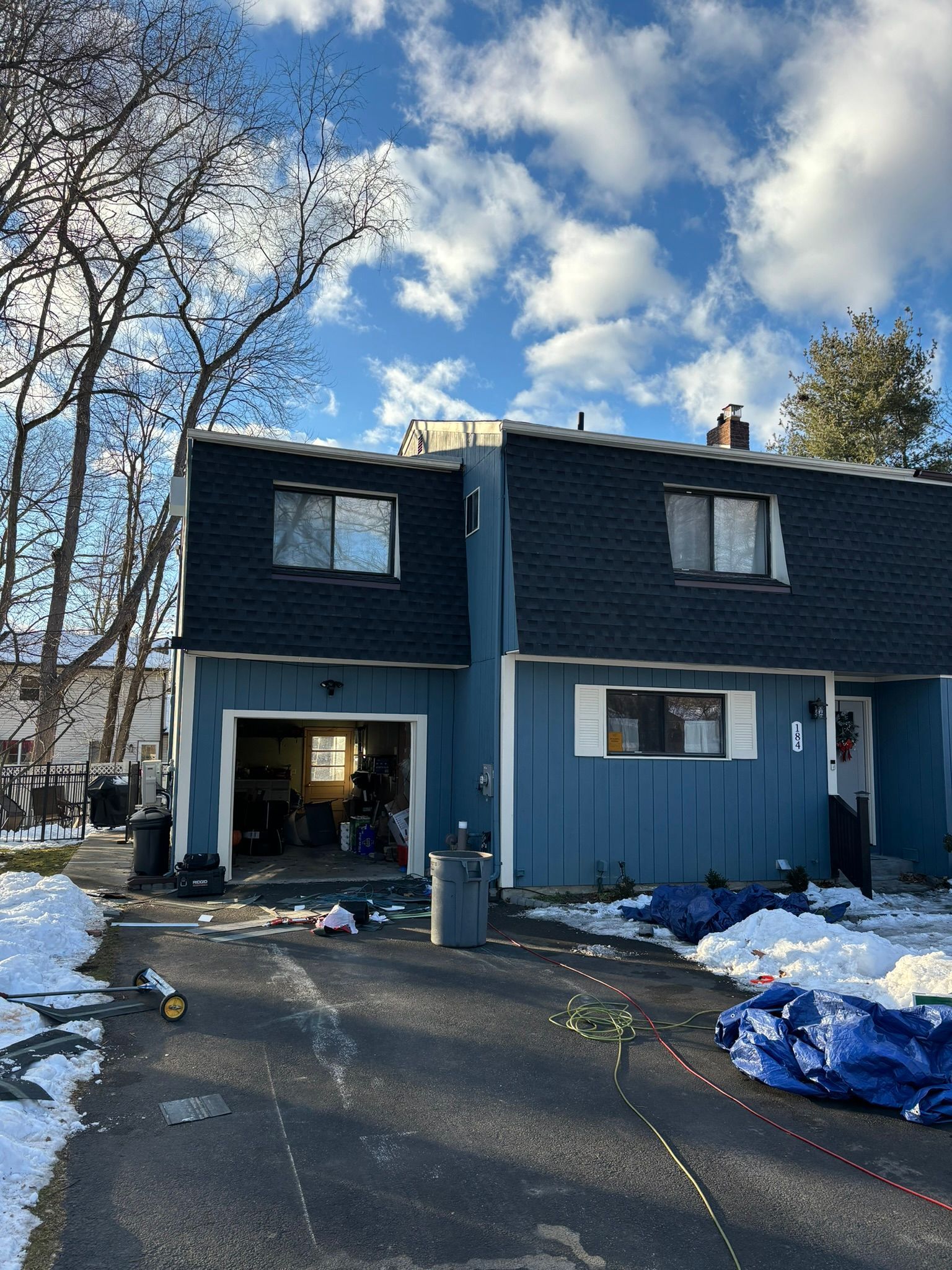 Blue townhouses under a partly cloudy sky; a partially open garage and snowy driveway.