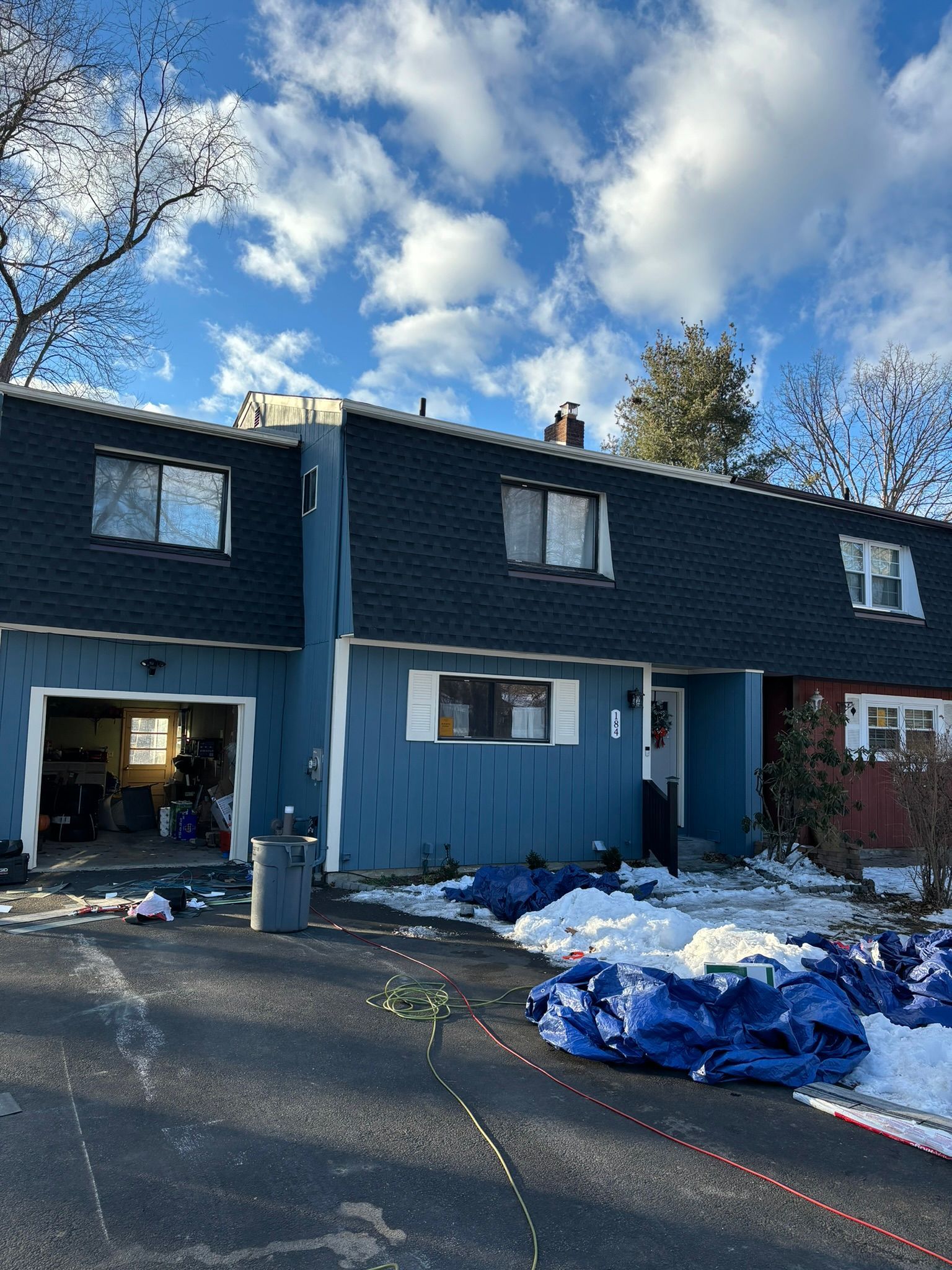 Blue row house with dark roof; snow on ground, blue tarps, sunny sky.