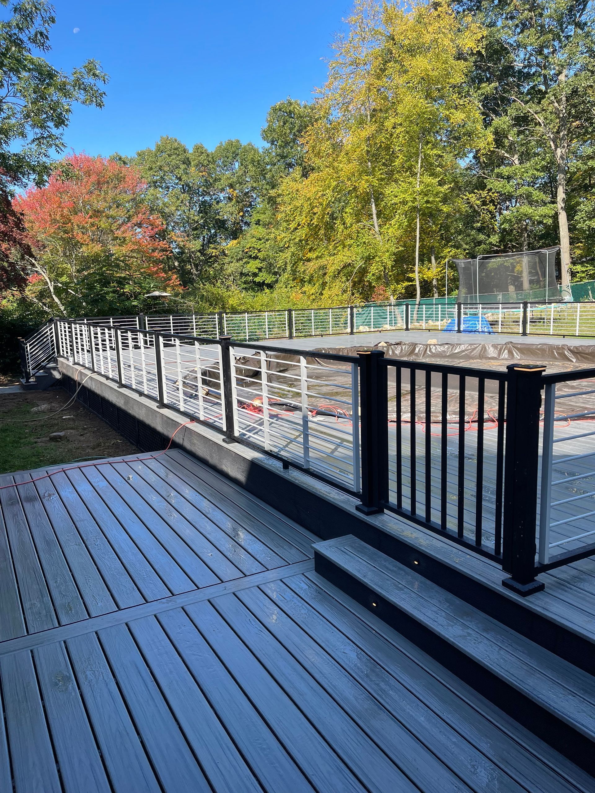 Deck with black railing, light gray composite boards, and view of trees with fall foliage.