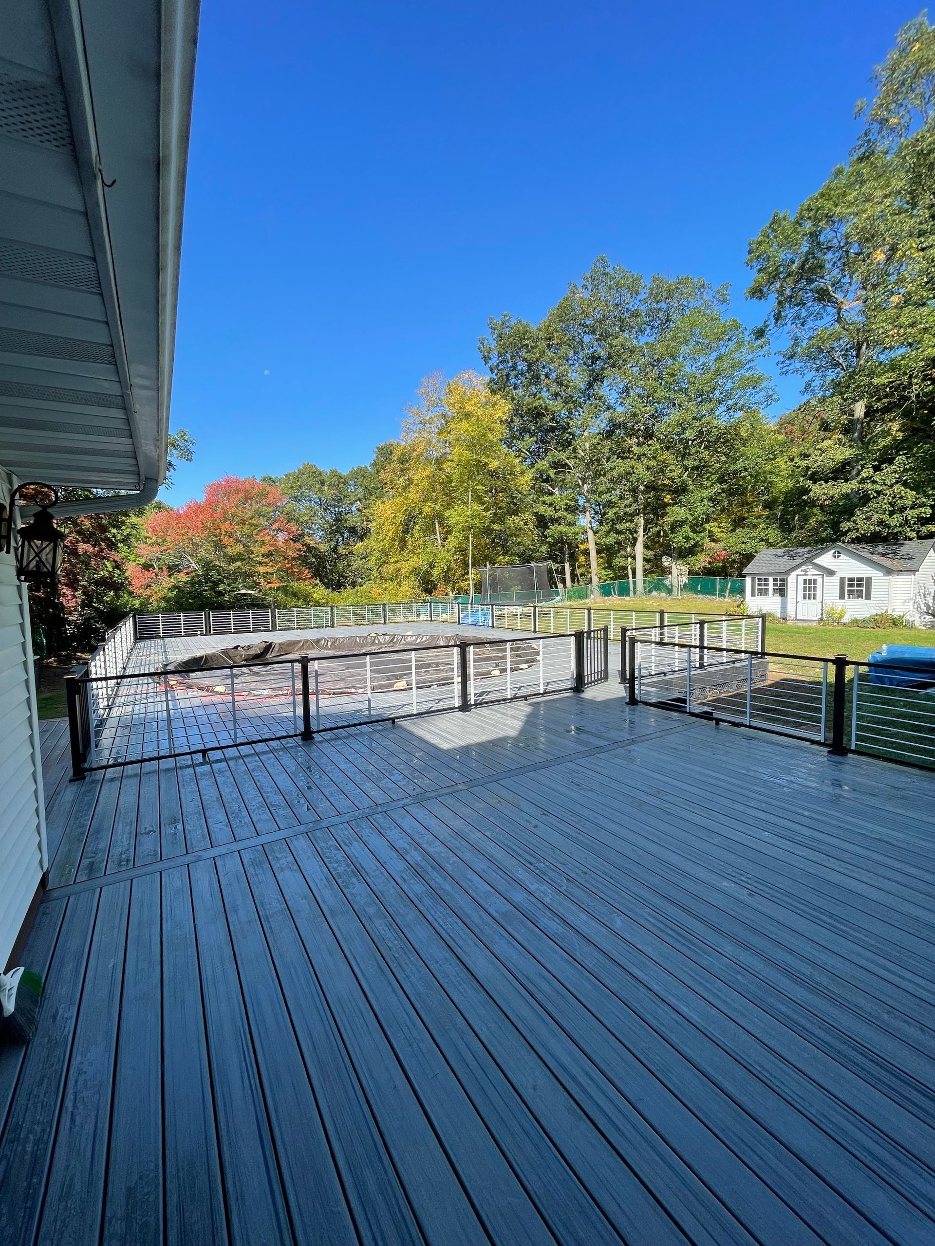 Large deck overlooking a pool area and trees under a clear blue sky.