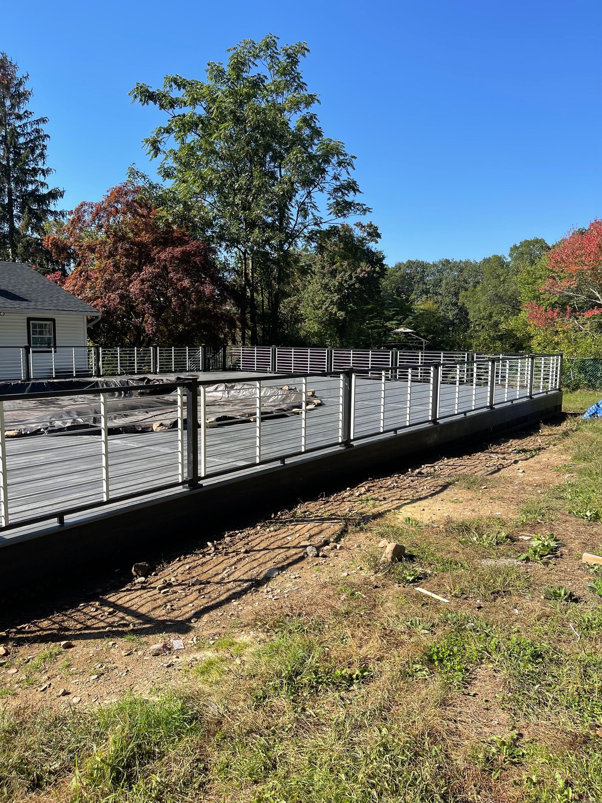 A dark-colored retaining wall with a decorative white fence in front.  Green grass and trees surround it under a blue sky.