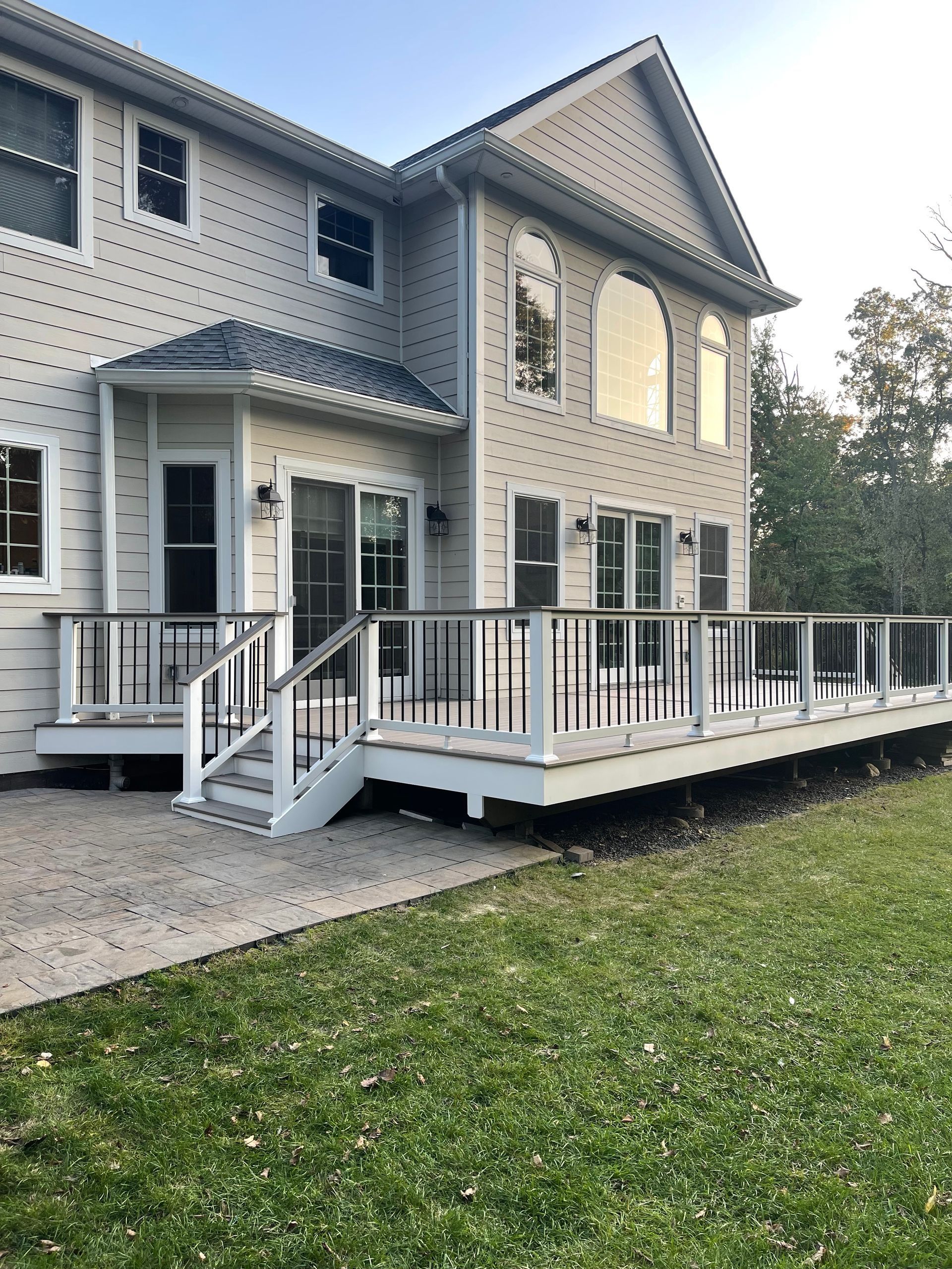 Back of a two-story beige house with a large wooden deck and a green lawn.