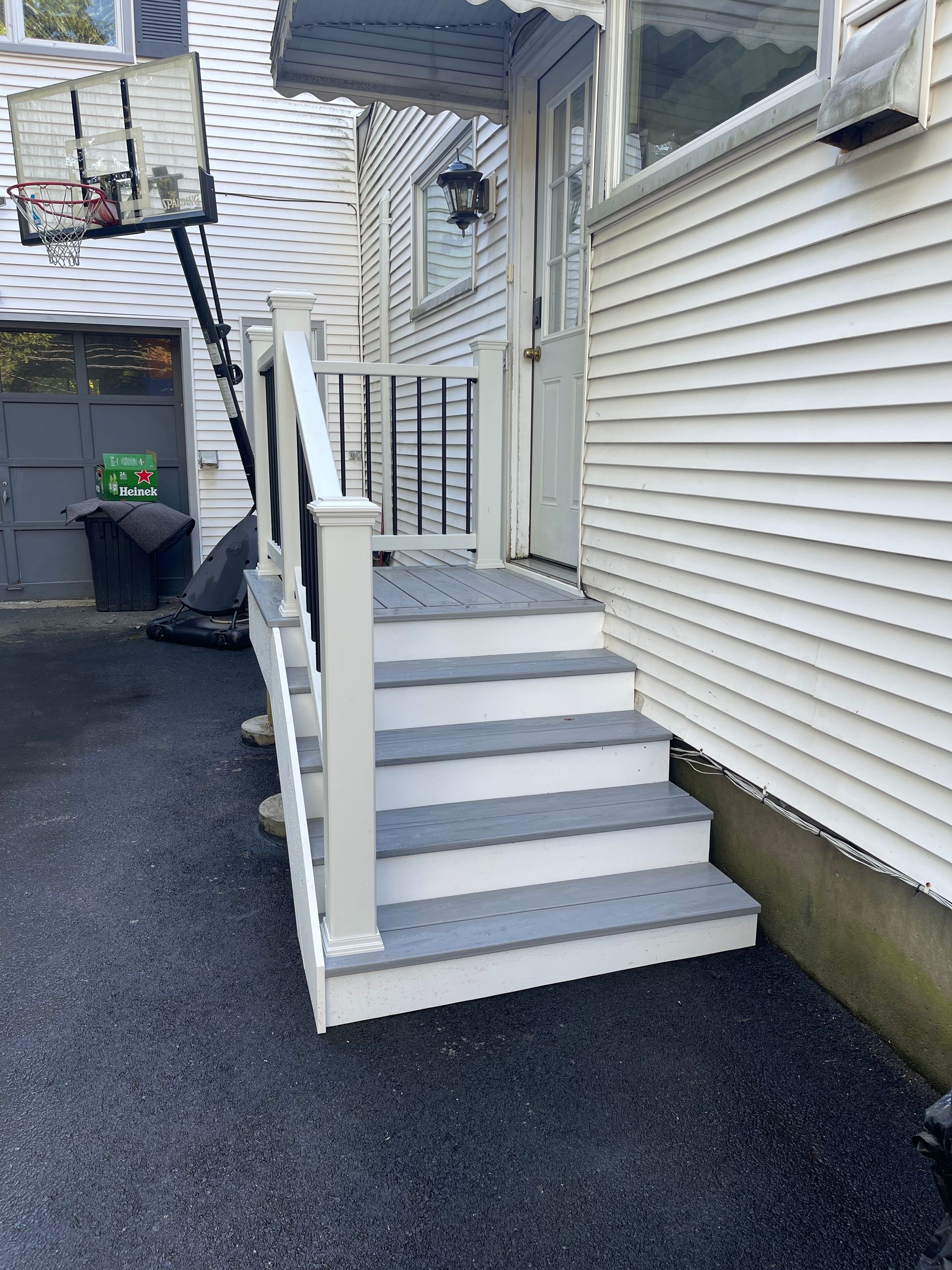 Exterior staircase leading to a house entrance. Gray steps, white railings, set against a white siding house and black asphalt.