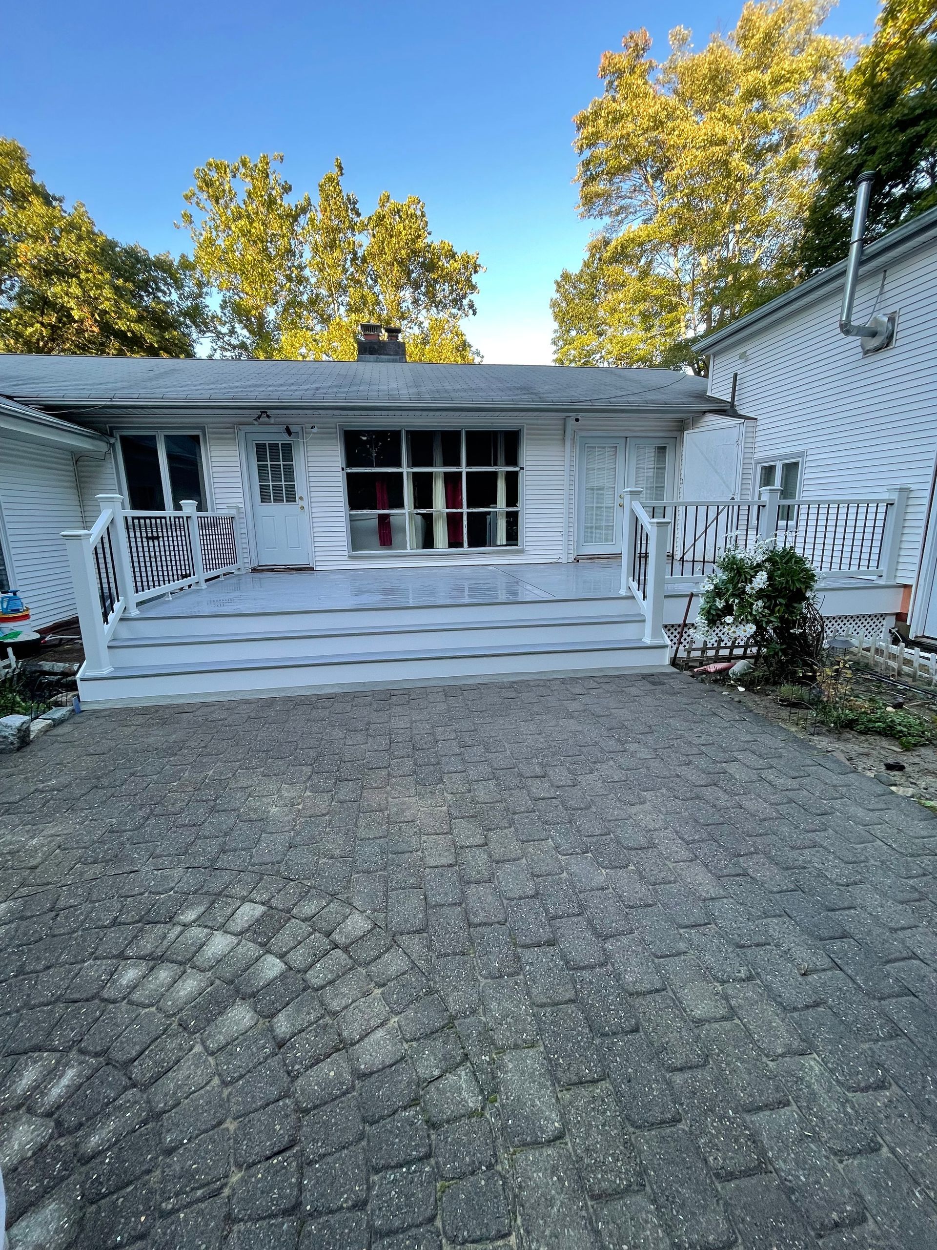 White house exterior with porch, steps, and brick driveway; trees in the background.