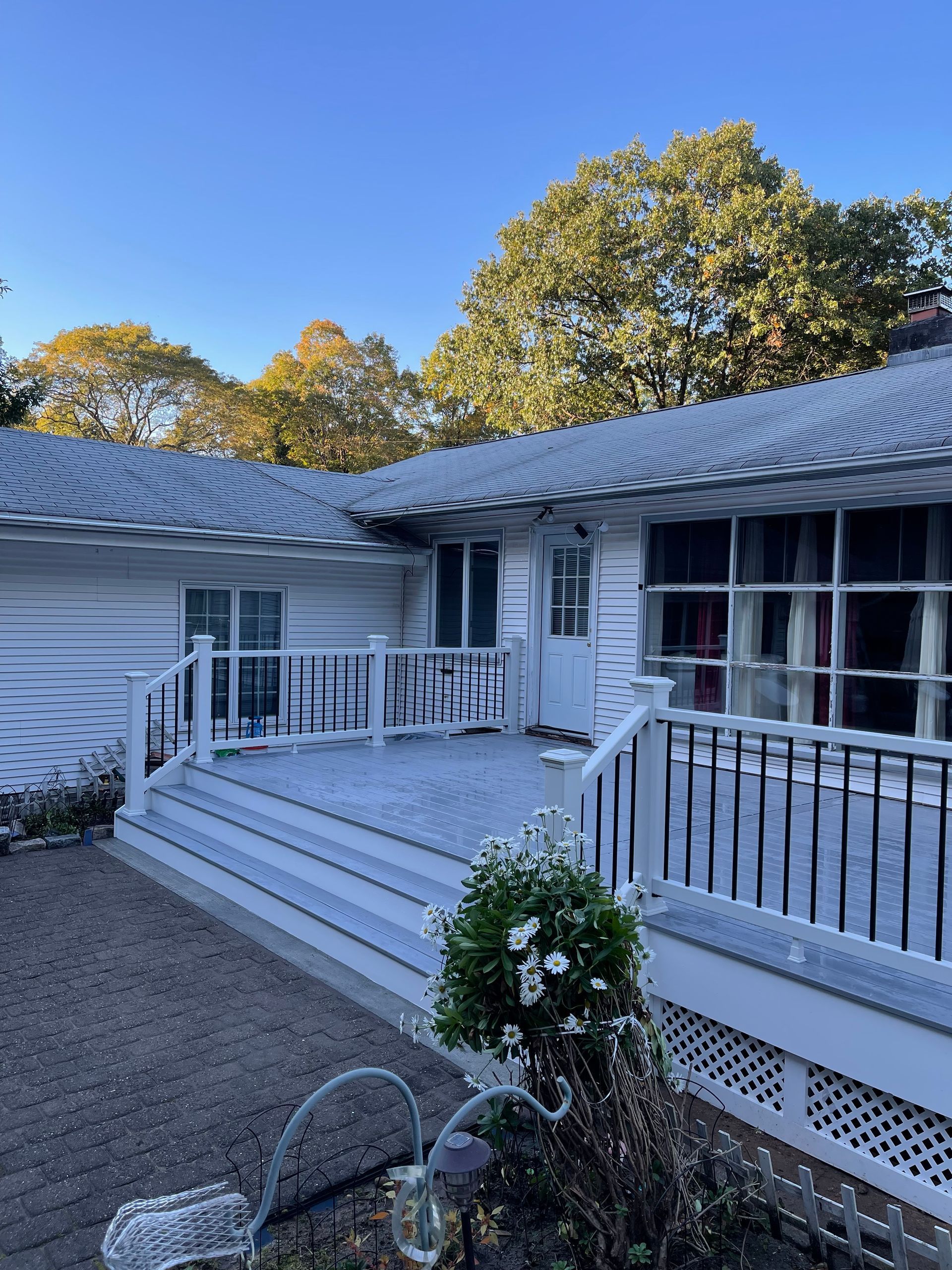 White house with deck and foliage against a blue sky.