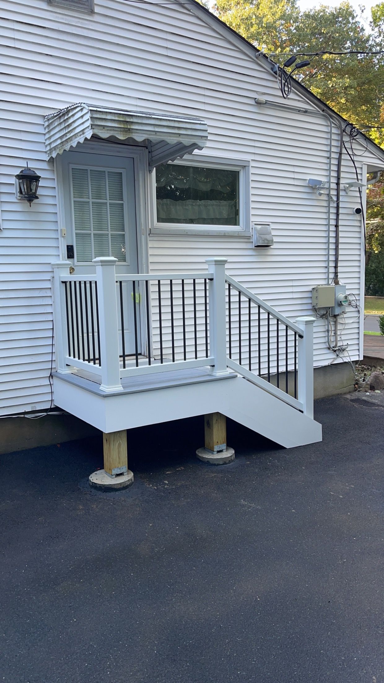 White house exterior with small porch, steps, and handrail; a door with an awning.
