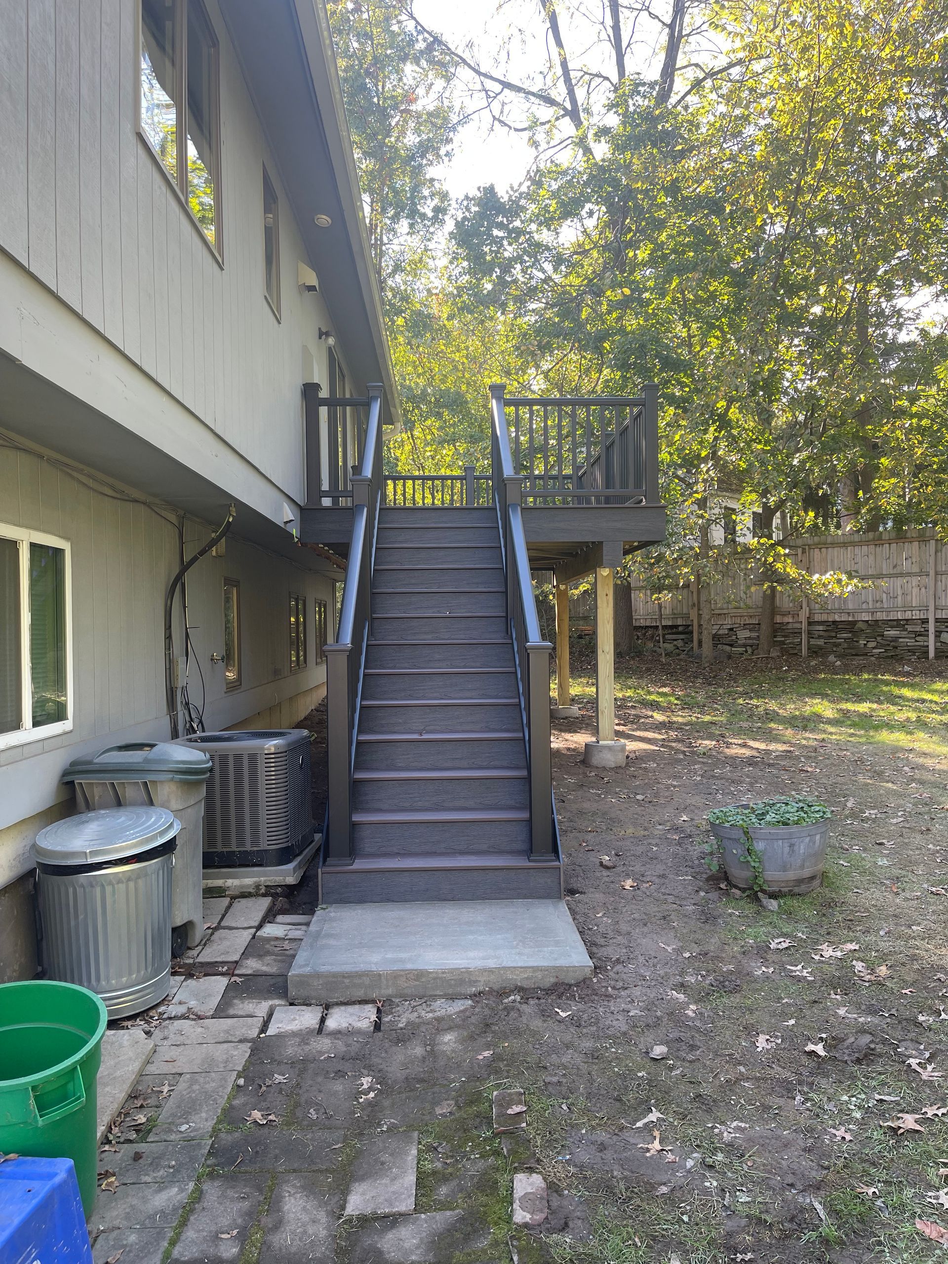 Backyard scene with stairs leading to a deck on a two-story house. Gray siding, surrounded by trees and grass.