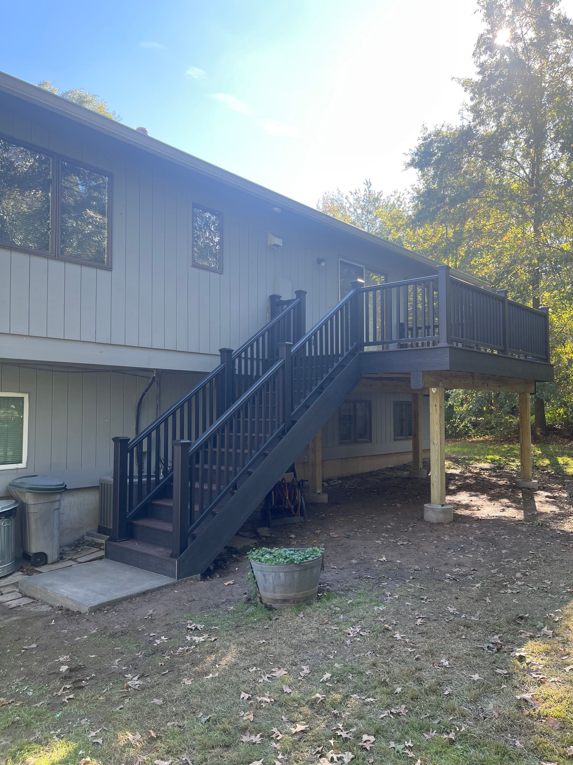 Two-story house with a wooden deck and stairs painted dark brown, set in a yard with trees.