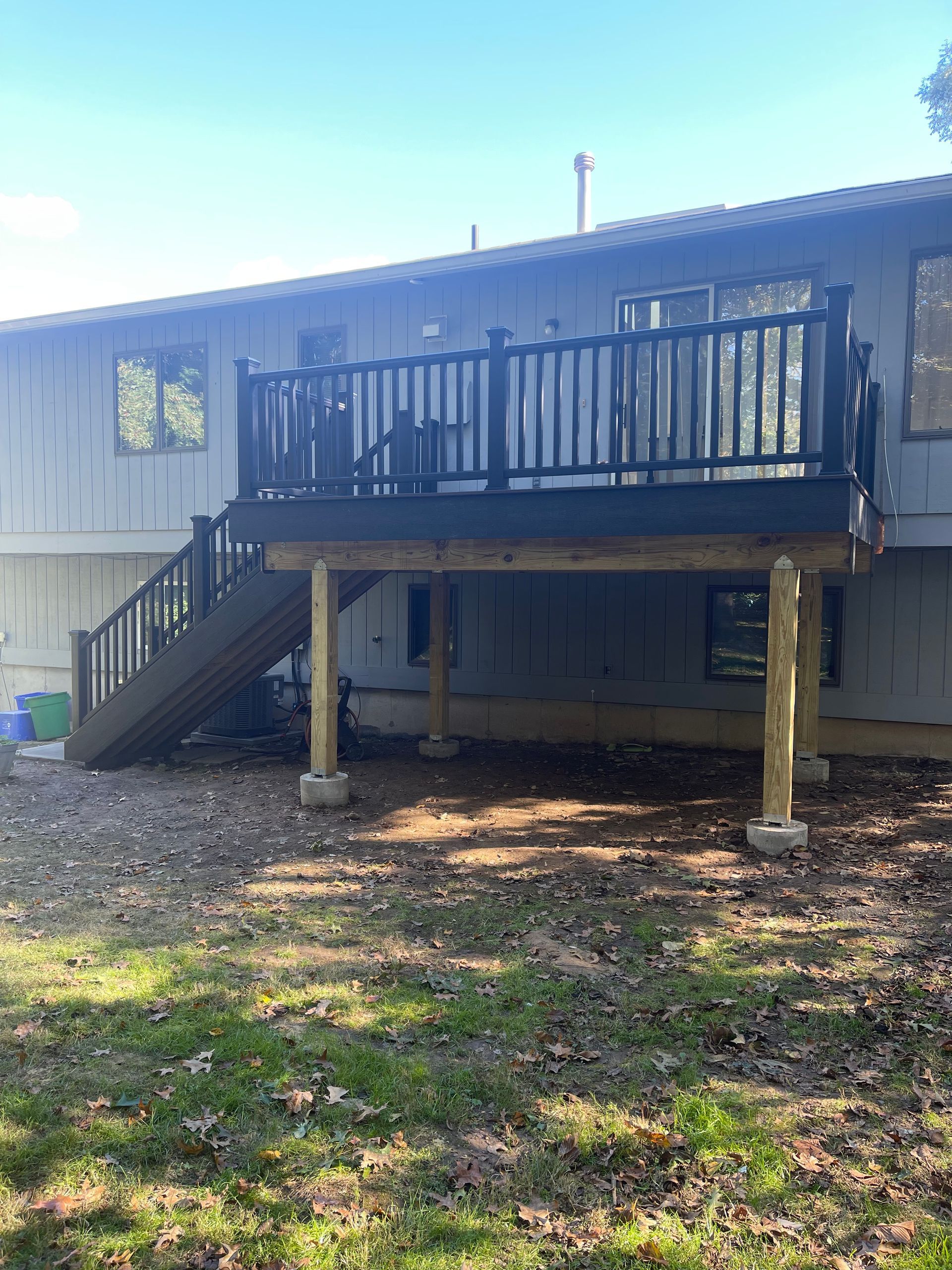Wooden deck on a house, with stairs and black railing. Sunlight illuminates the yard below.