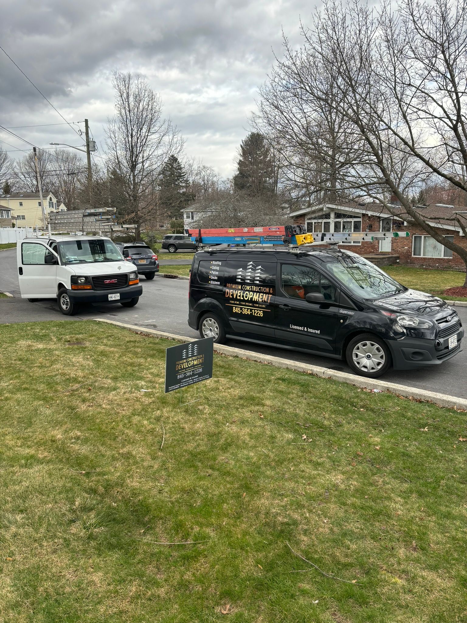 White van and black van parked on a residential street; overcast sky.