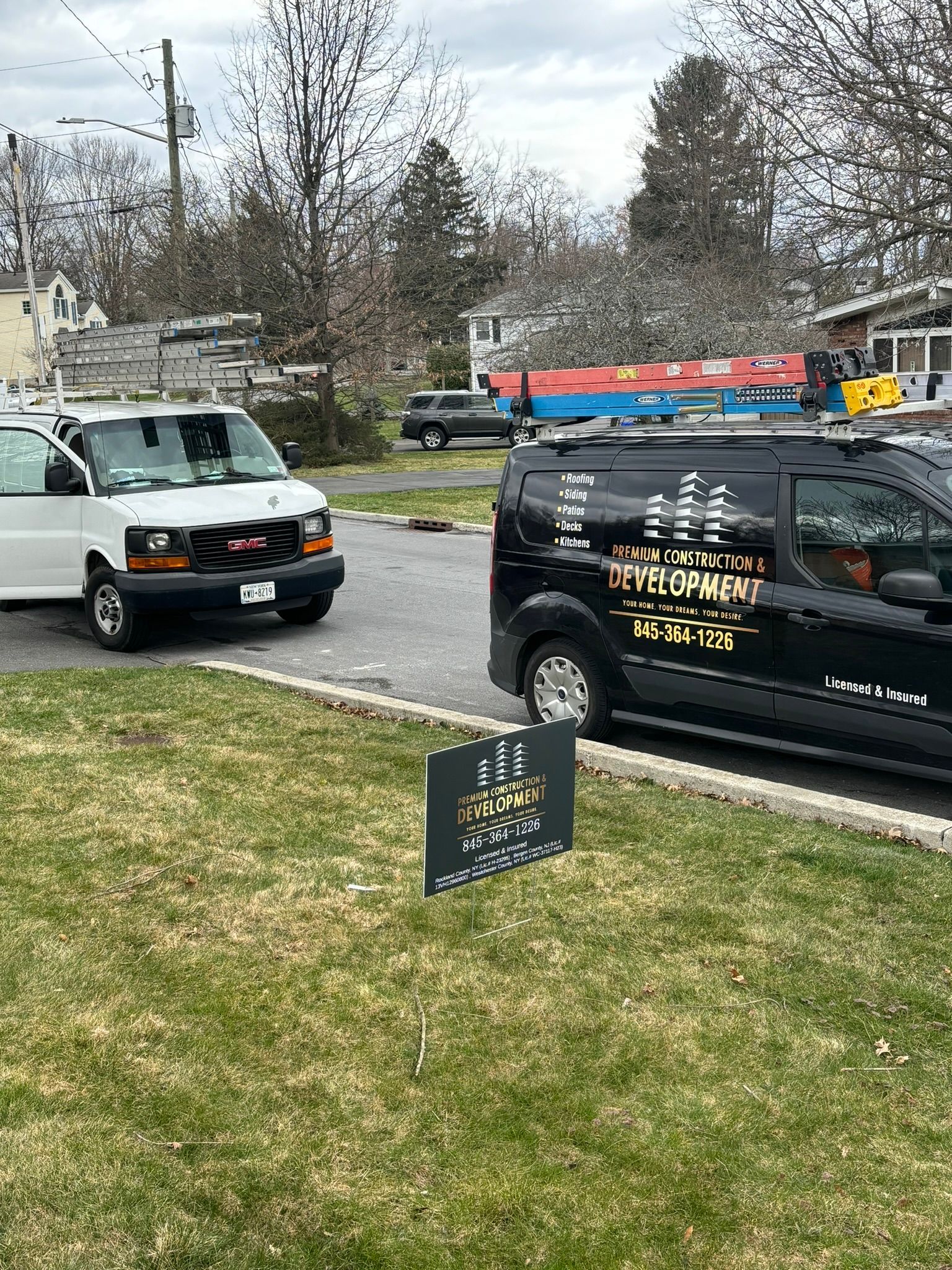 Two work vans parked on a residential street. A sign is in the foreground.