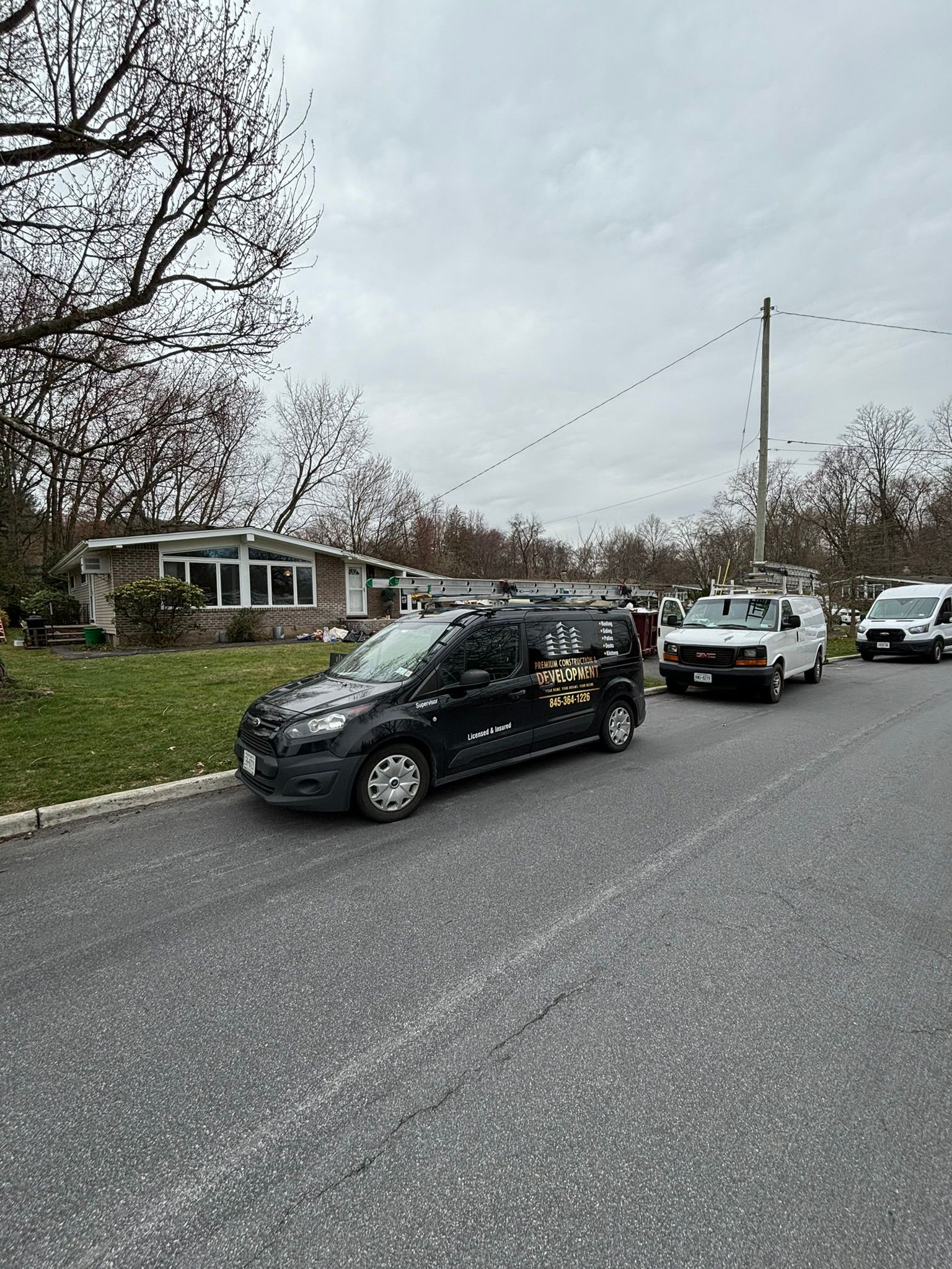 Black van with logo parked on street, two other vans behind it near house. Cloudy sky.
