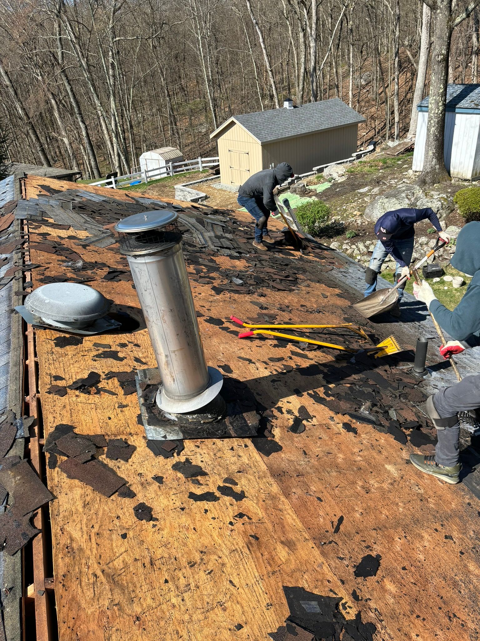 Workers repairing a roof with a chimney. The roof is old, brown, and has debris.