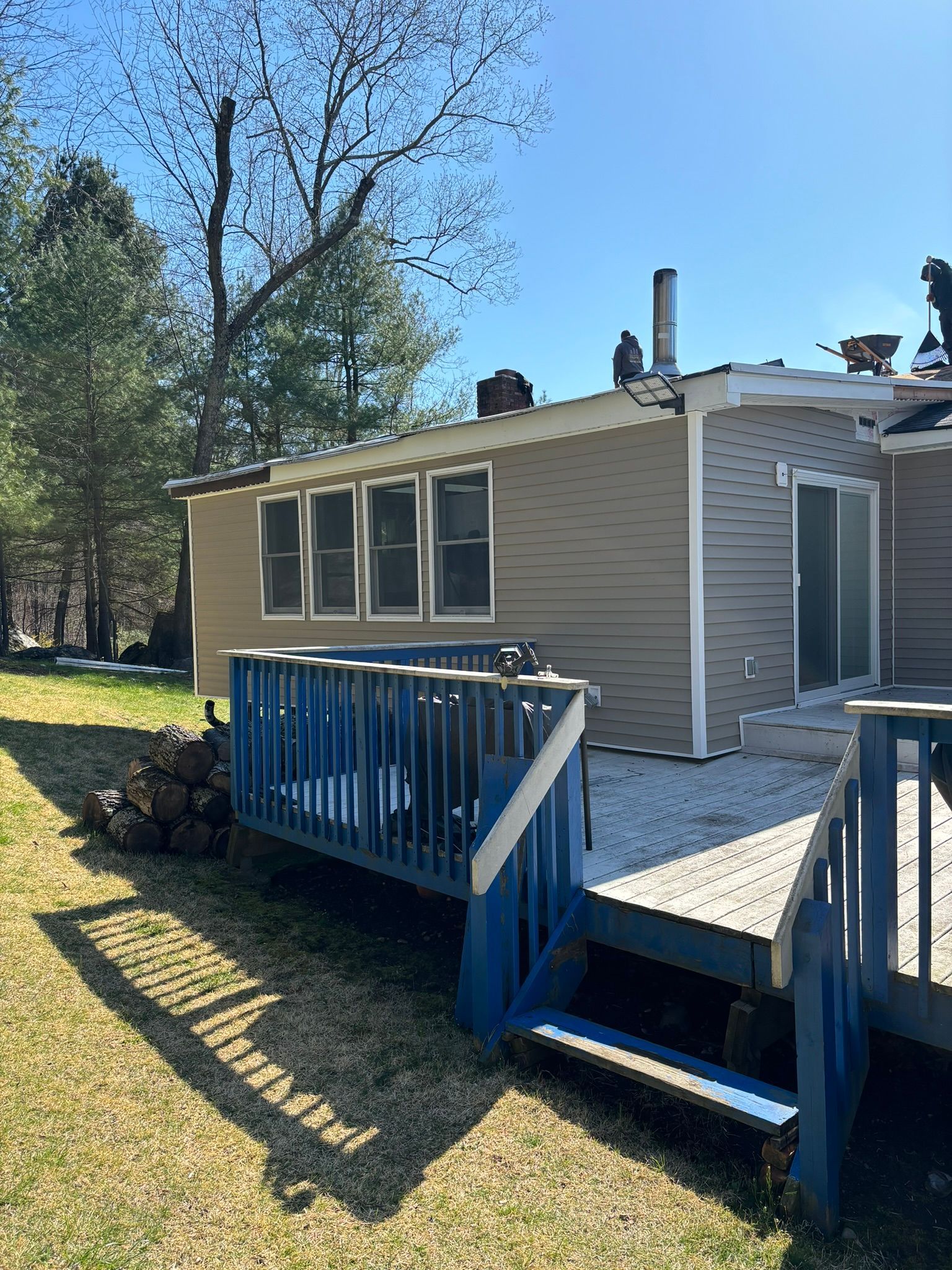 Deck with blue railings and siding on a light brown house with a blue sky.