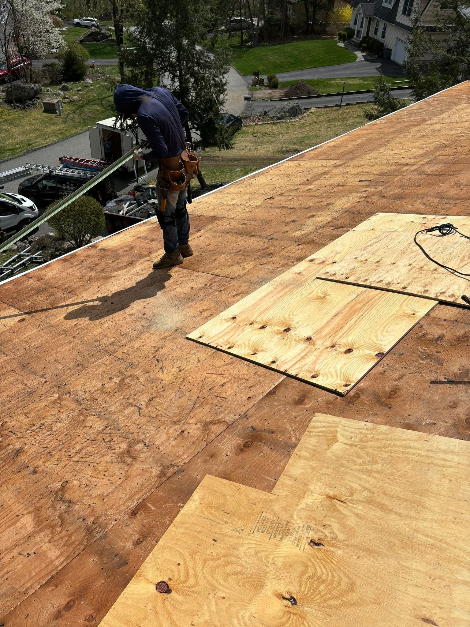 Roofer standing on a roof with plywood, installing or repairing shingles on a sunny day.