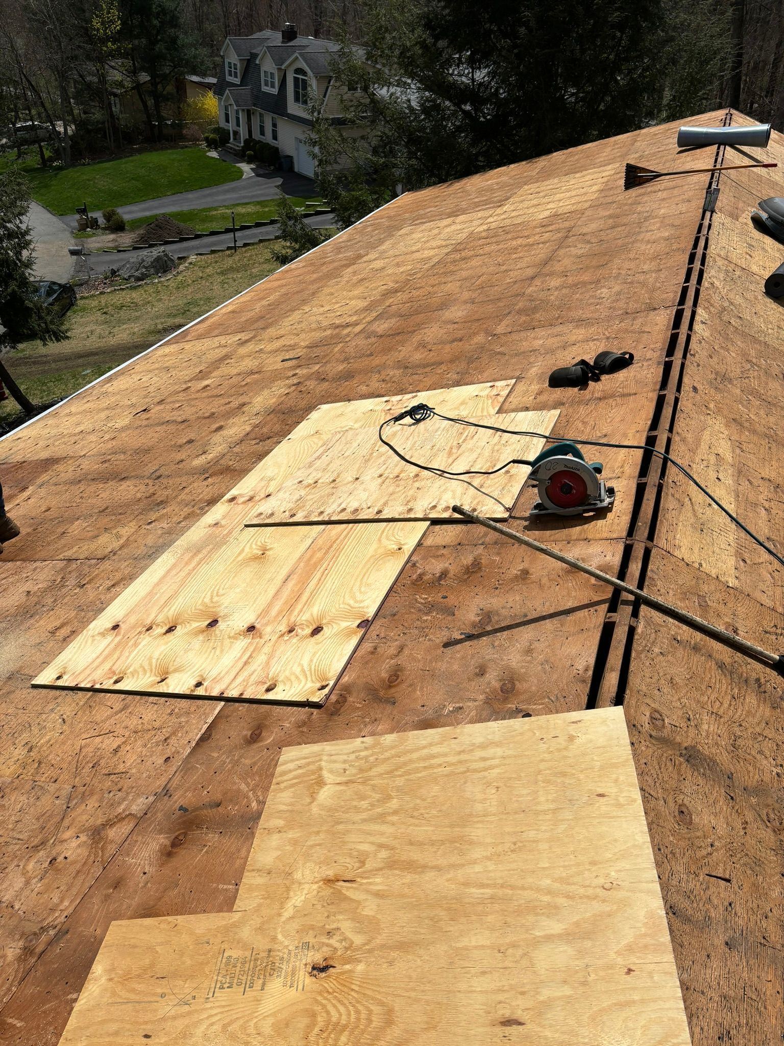 Rooftop with plywood being replaced, circular saw, sunny day, residential background.