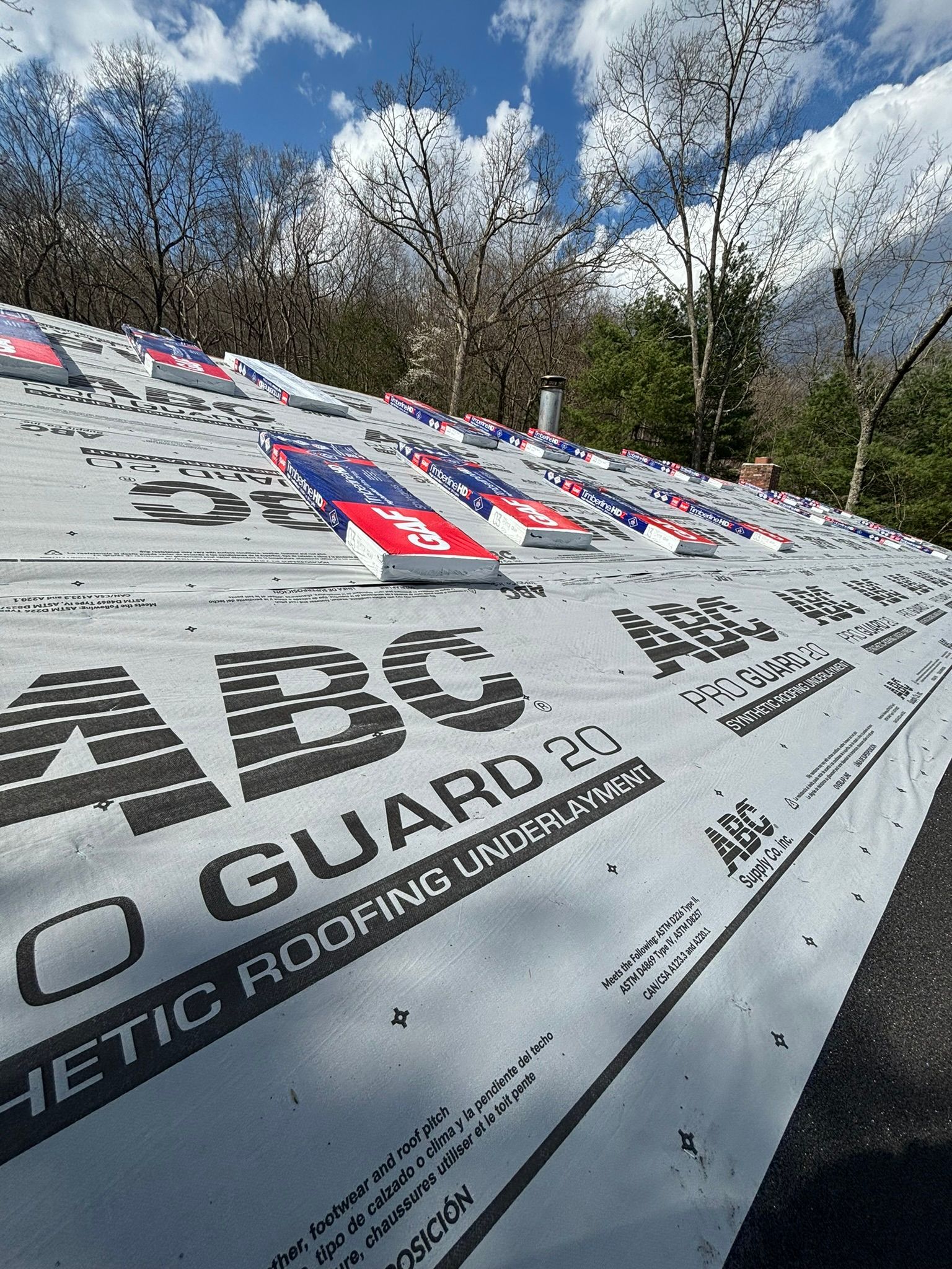 Roof with synthetic underlayment and metal brackets, under a blue sky.