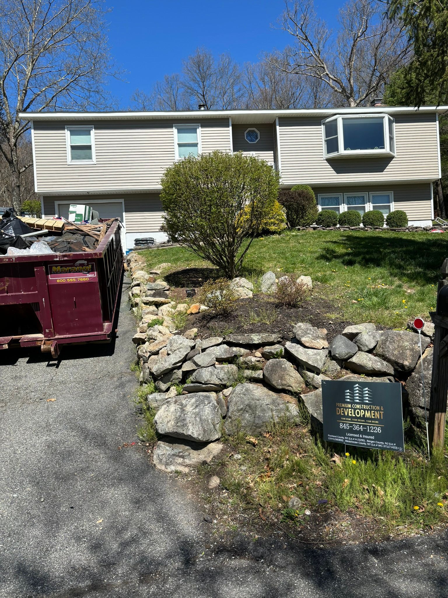 Two-story house with a stone retaining wall and a dumpster in the driveway.