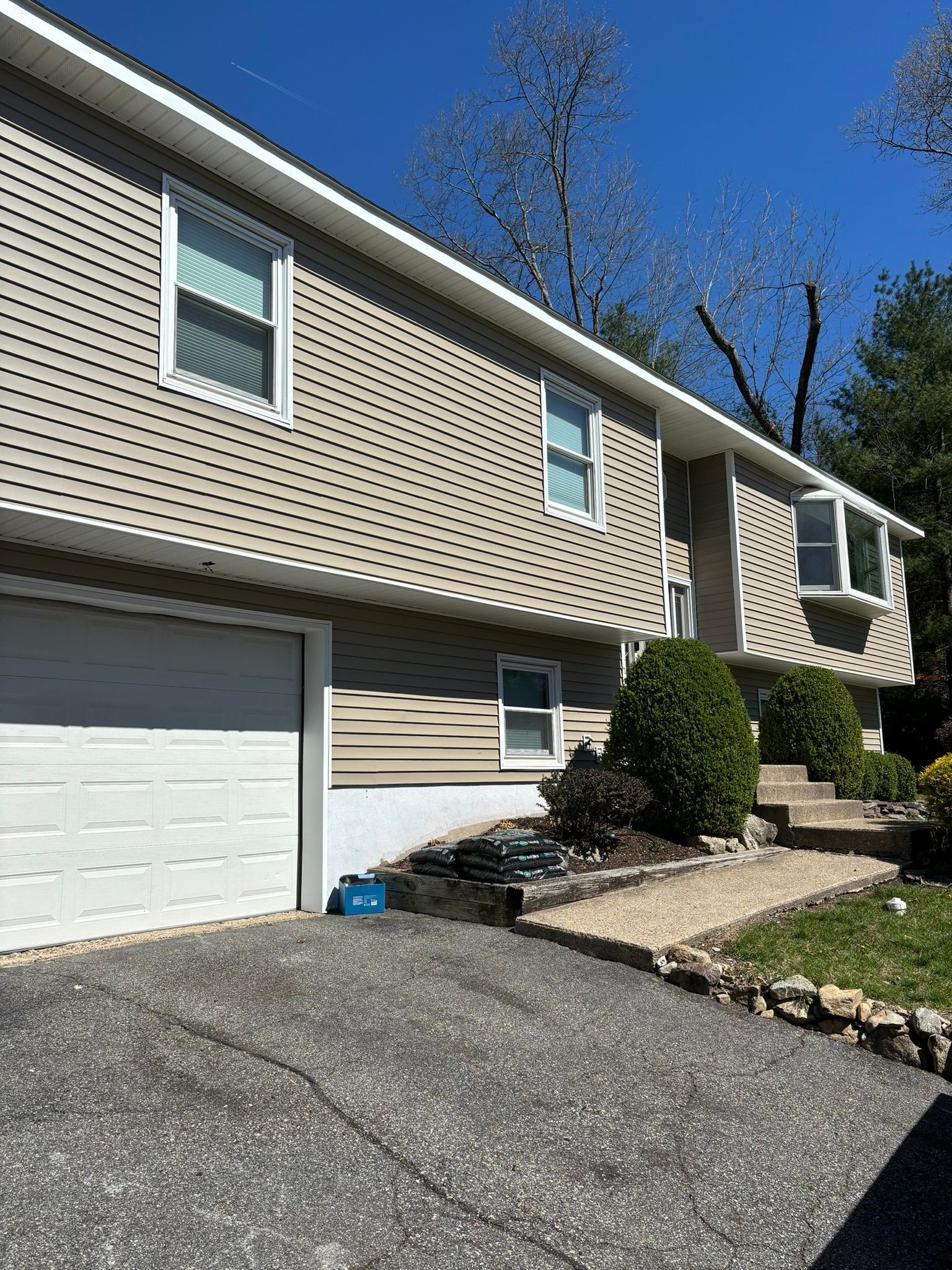 Two-story house with tan siding, white trim, and a gray driveway.  A small concrete walkway leads to the front door.