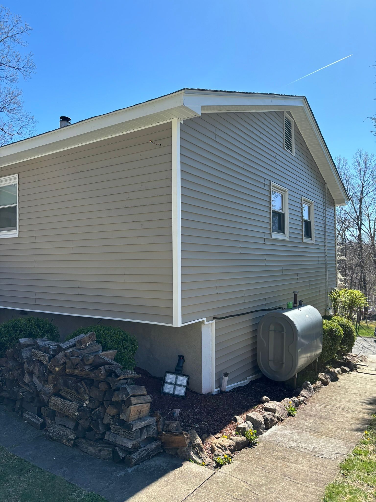Beige house with white trim, oil tank, and rock border under a blue sky.