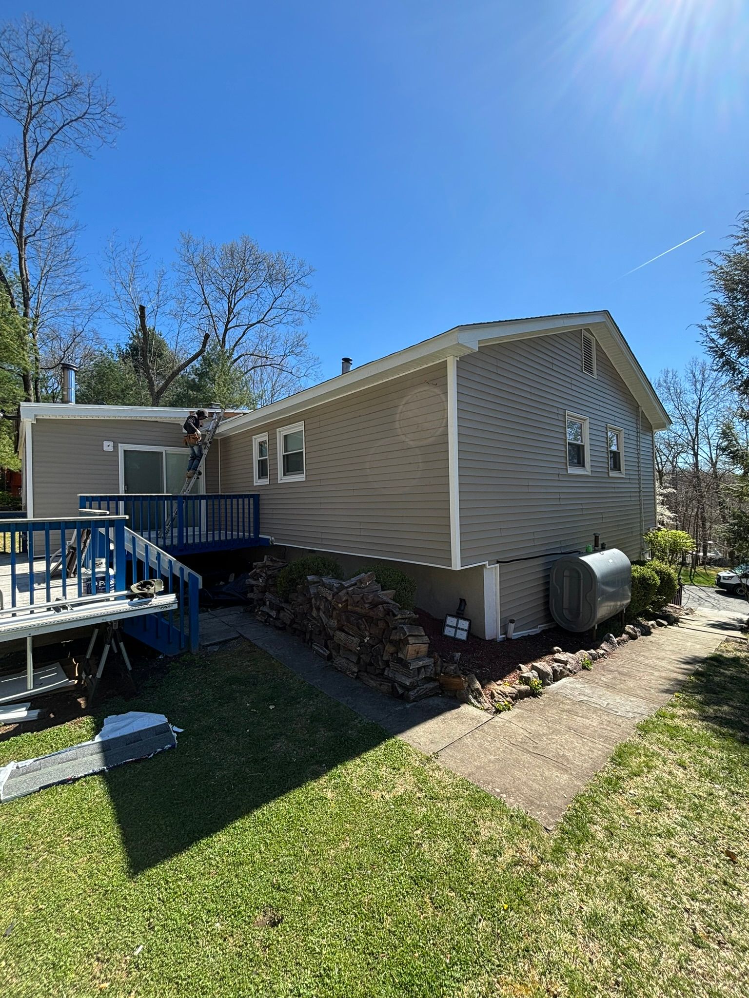 Side view of a house with light brown siding, blue deck, and a sunny blue sky.