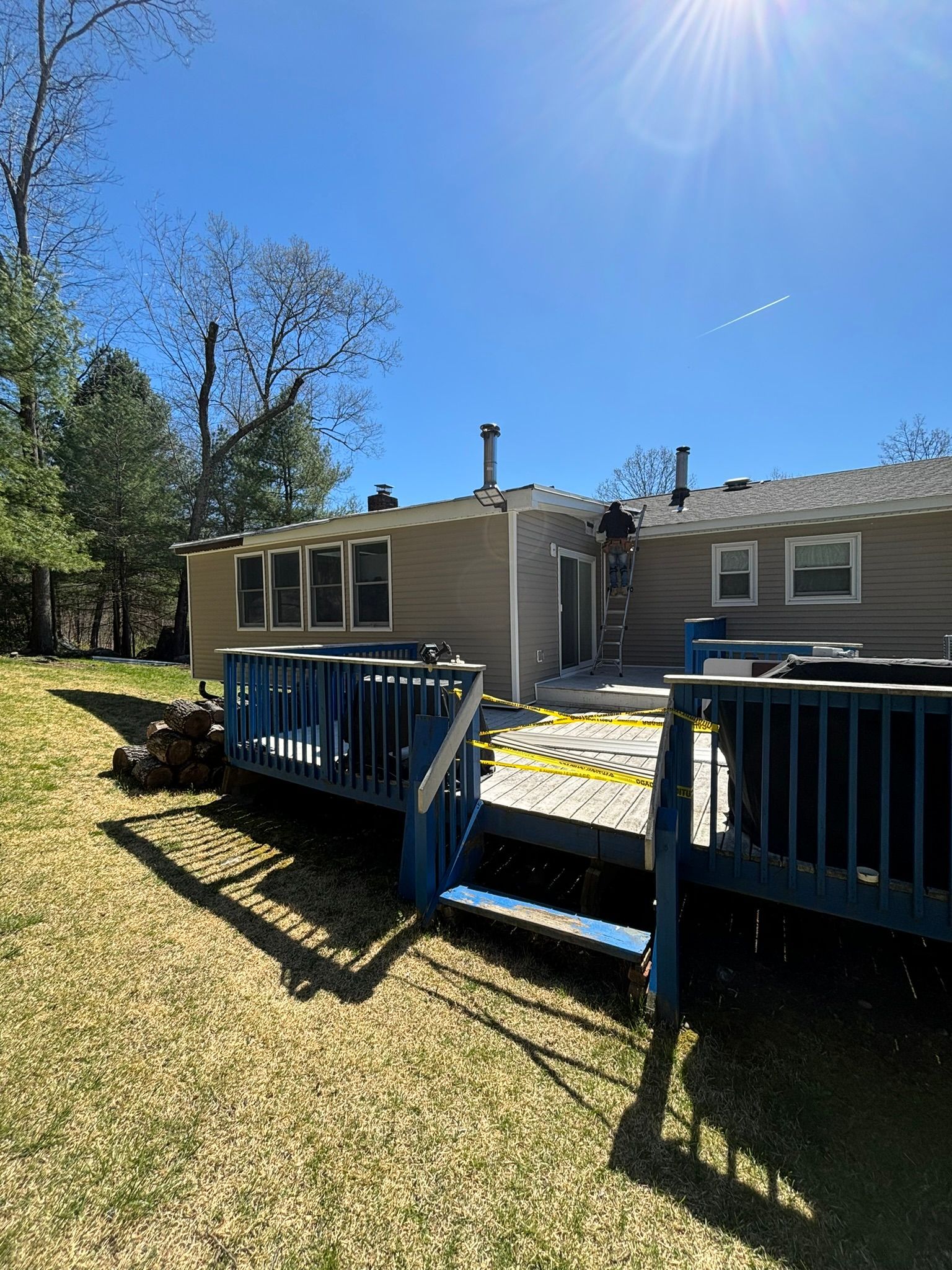 Backyard view of a beige house with a wooden deck, blue trim, and a ladder on the roof.