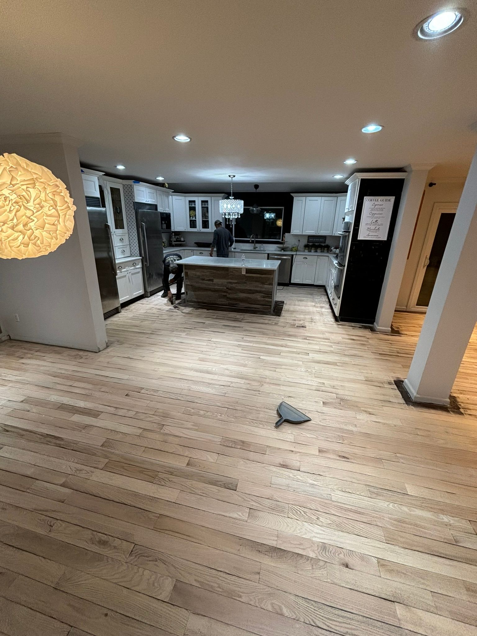 Kitchen with new wood flooring being installed; white cabinets, island, and appliances.