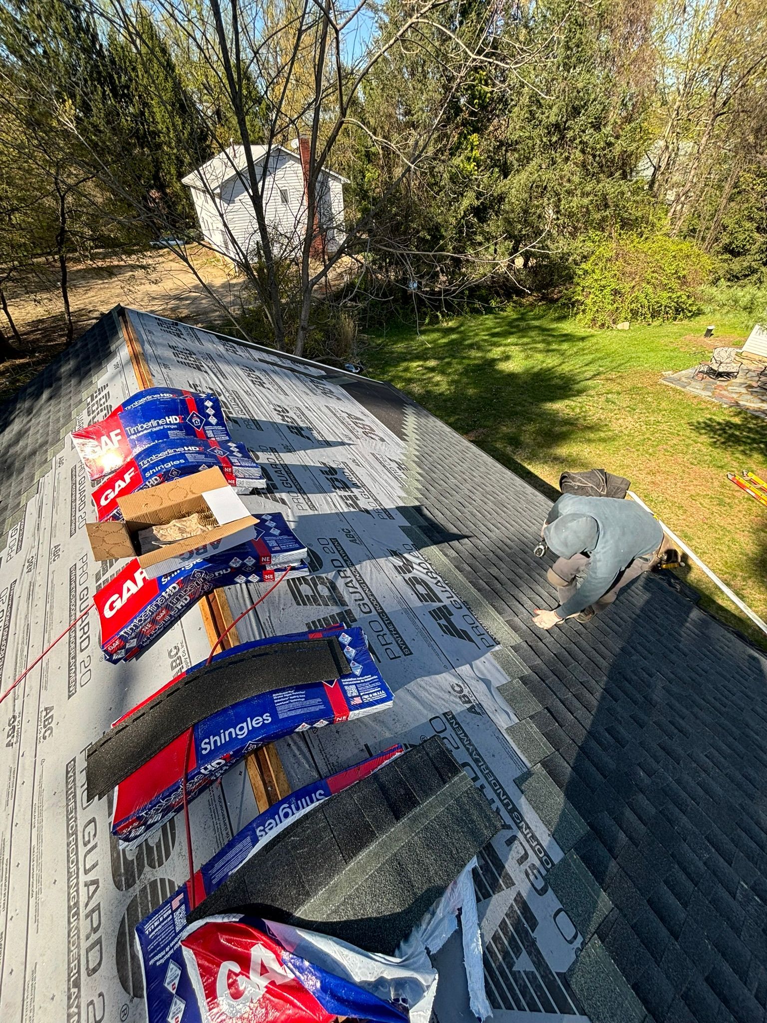 Roof with packaged shingles, tarpaper, and tools, outdoors on a sunny day.