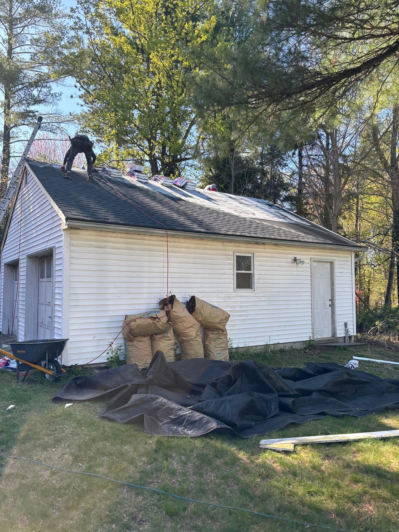 Person working on a white garage roof; debris and bags of materials on the ground.