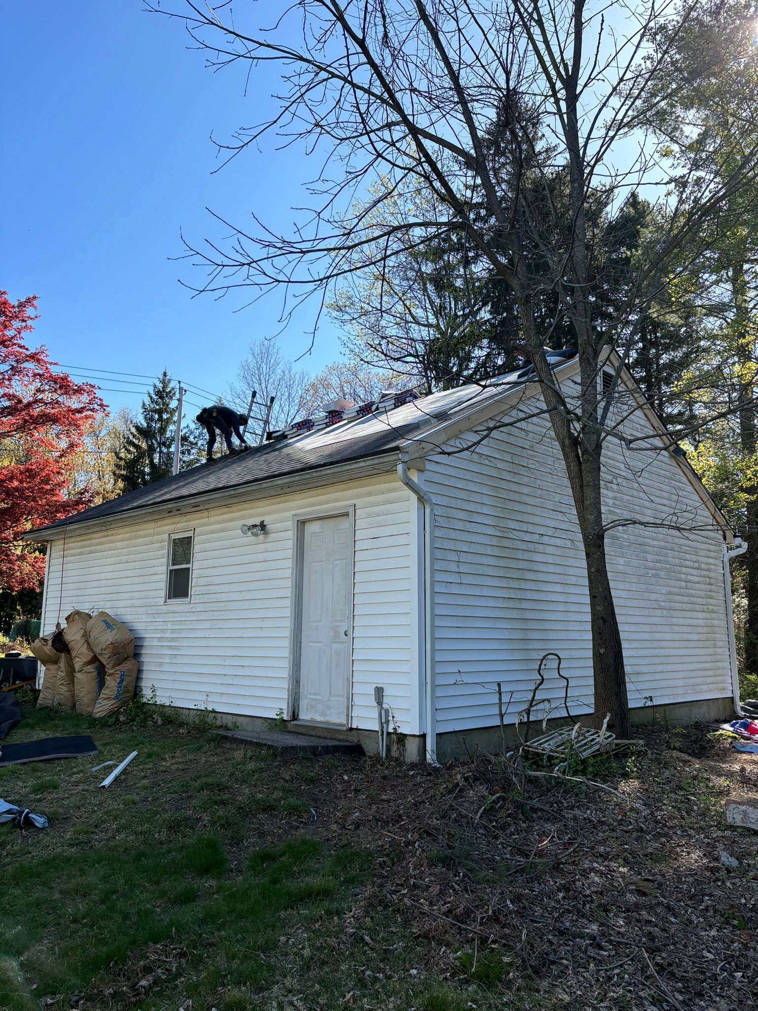 White, single-story building with a white door and small window under a blue sky, tree on the right.