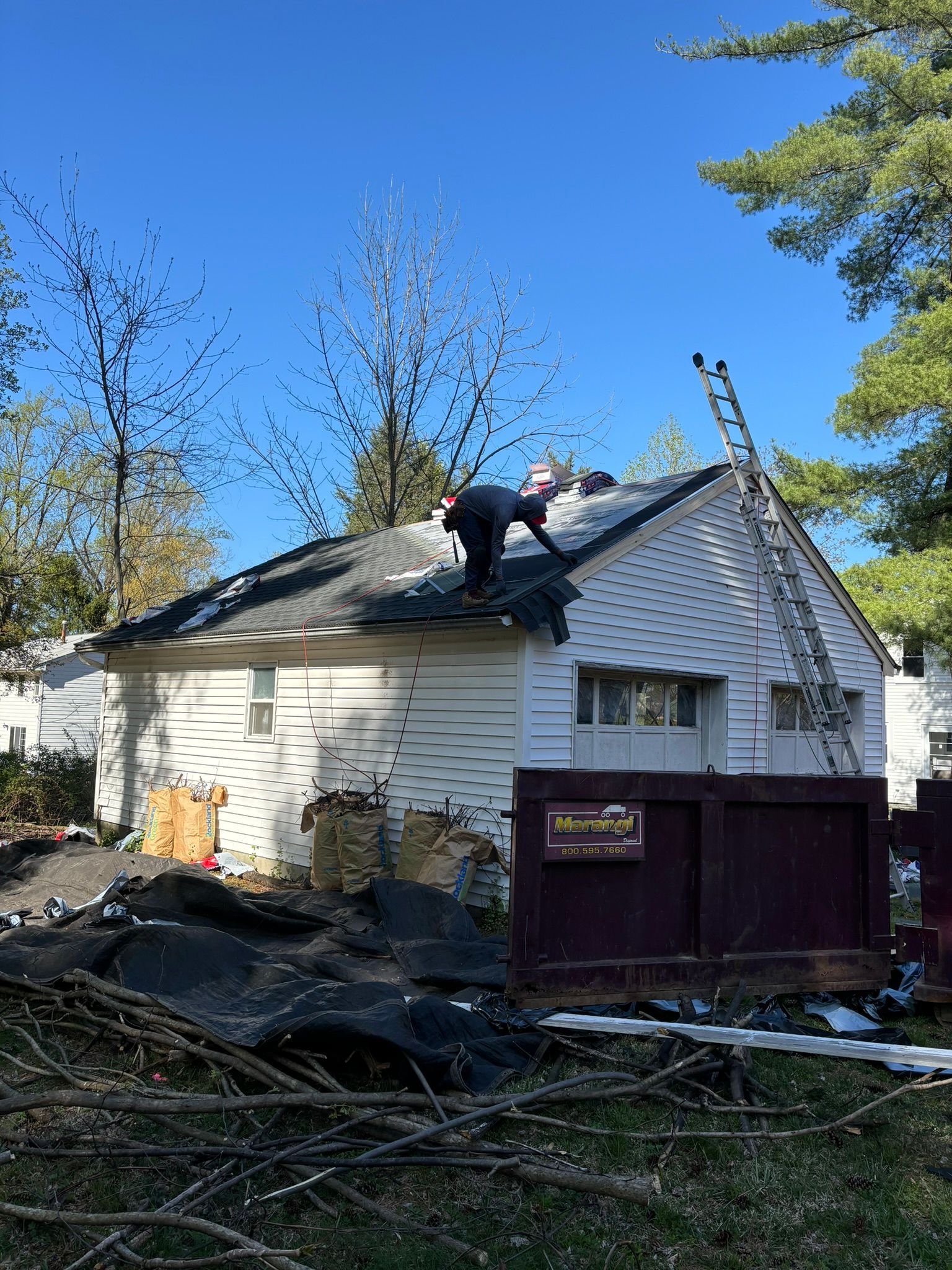 Person on a roof, near a ladder, working on a white house with a blue sky background.