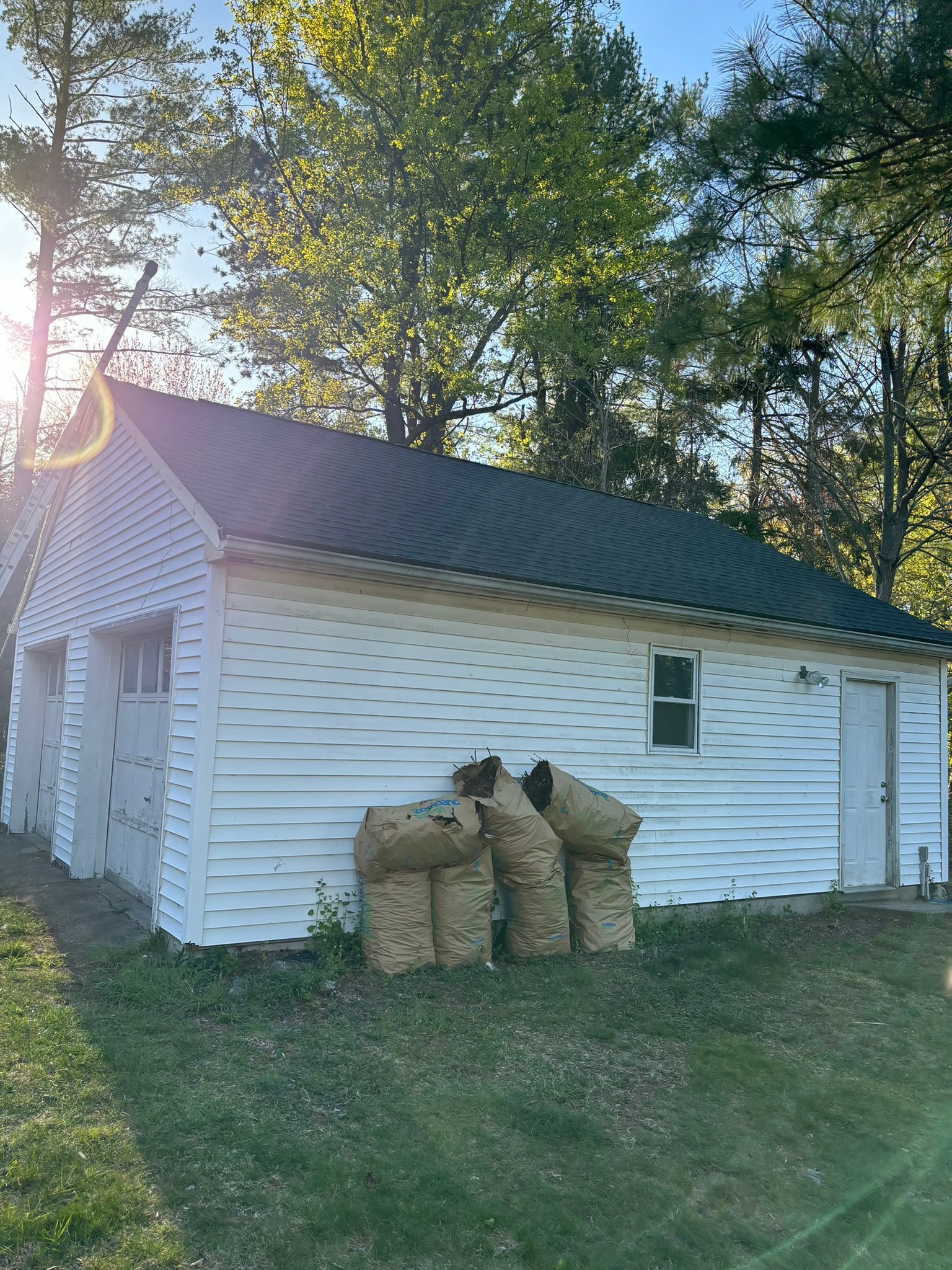 White garage with green metal roof; bags stacked in front.