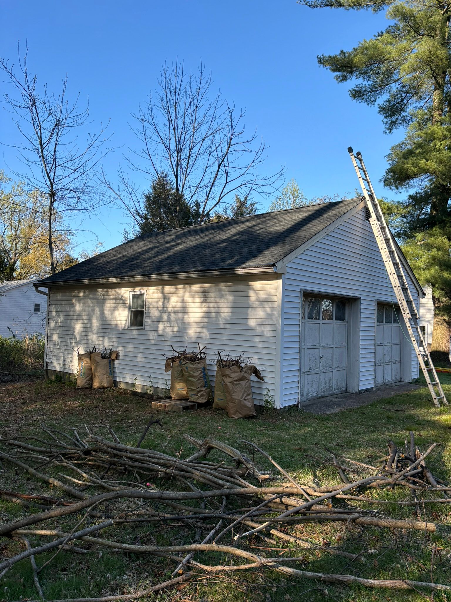 White building with a dark roof and a ladder. Logs are stacked near the building.
