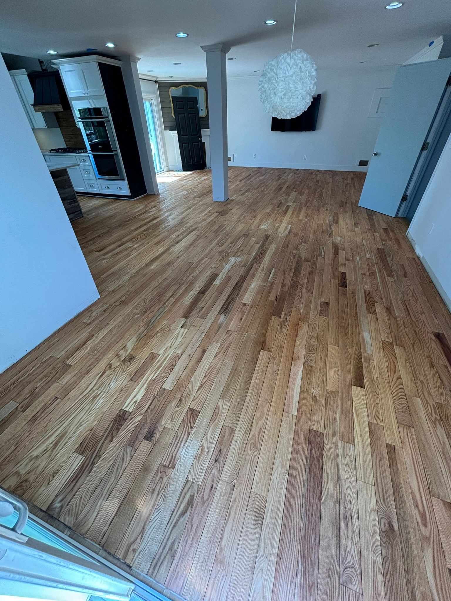 Hardwood flooring in a room with white walls, kitchen appliances, and a decorative light.