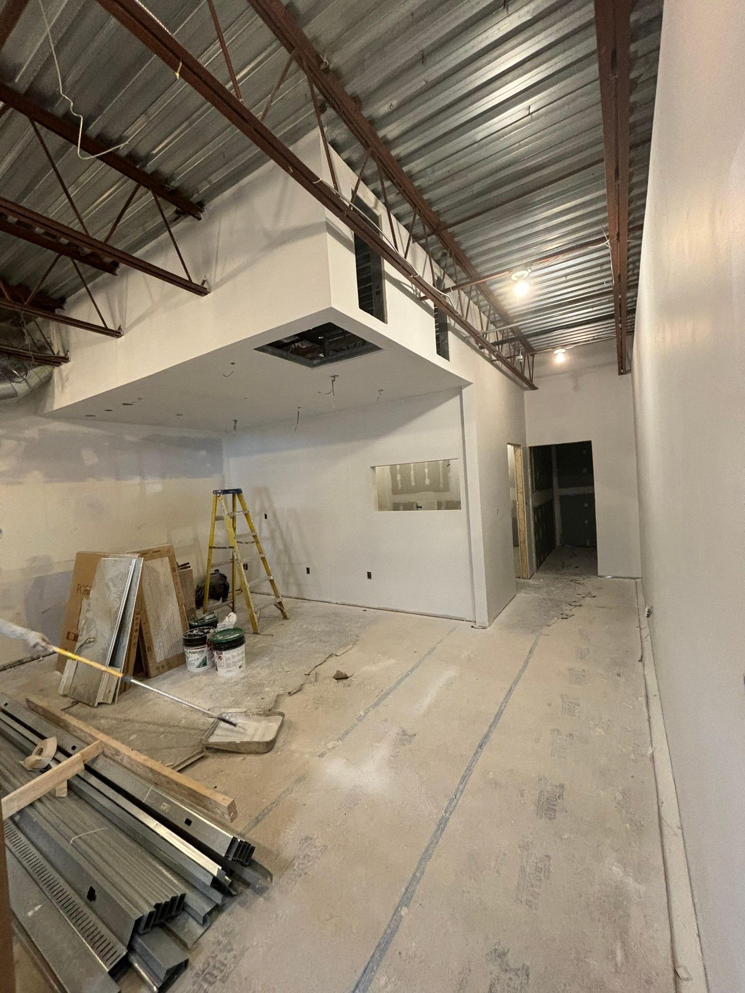 Interior construction site with exposed metal beams, drywall walls, and concrete floor.