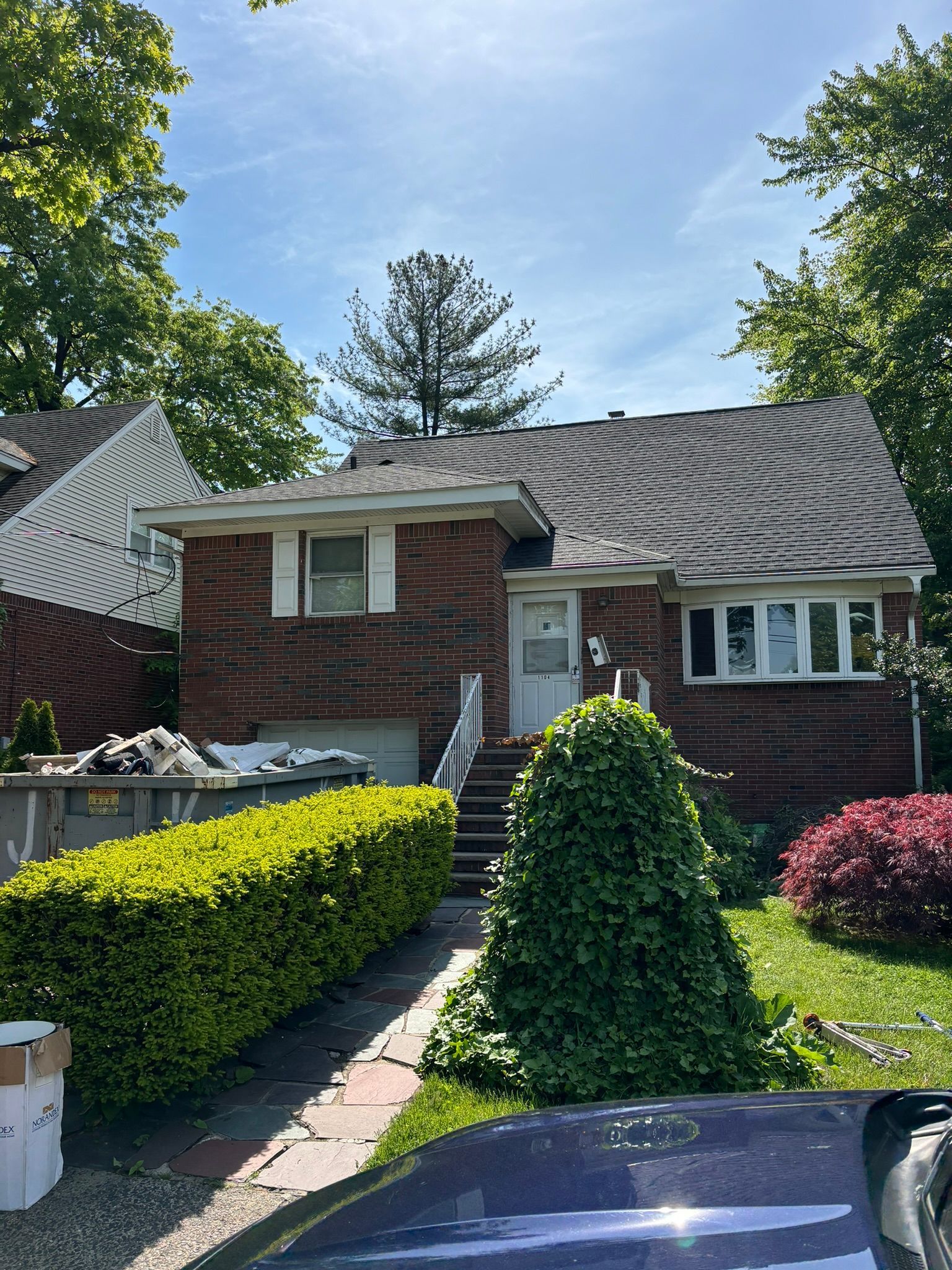 Brick house with steps, hedge, and a blue sky in the background.