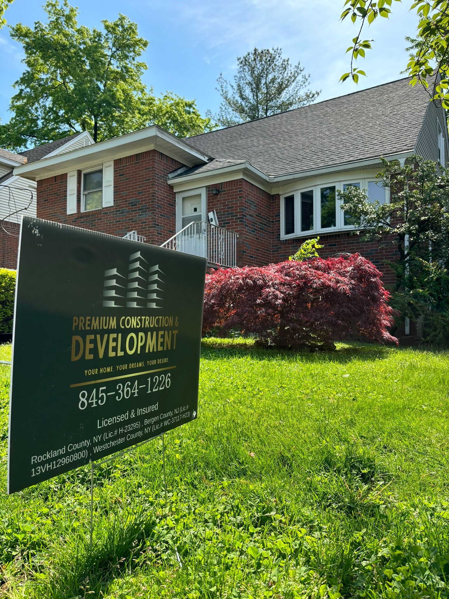 Green sign in front yard of a brick house; 