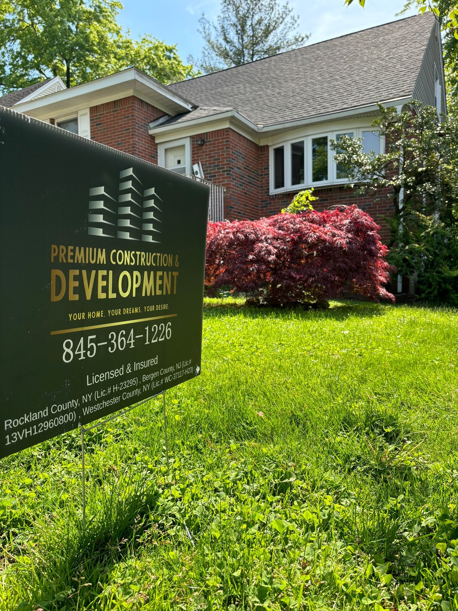 Sign for Premium Construction Development in front of a brick house with a green lawn.
