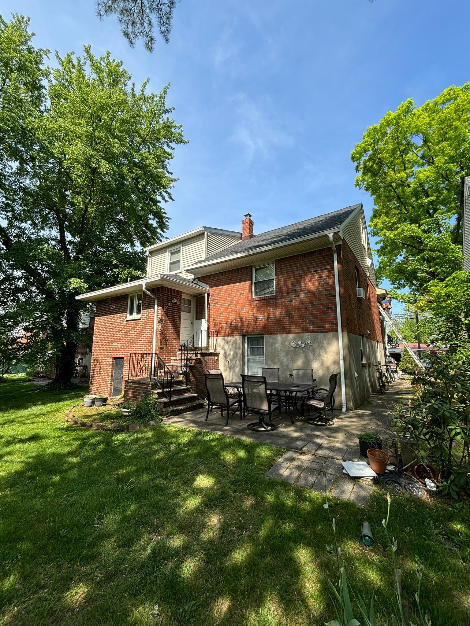 Red brick house with patio, green lawn, trees, and blue sky.