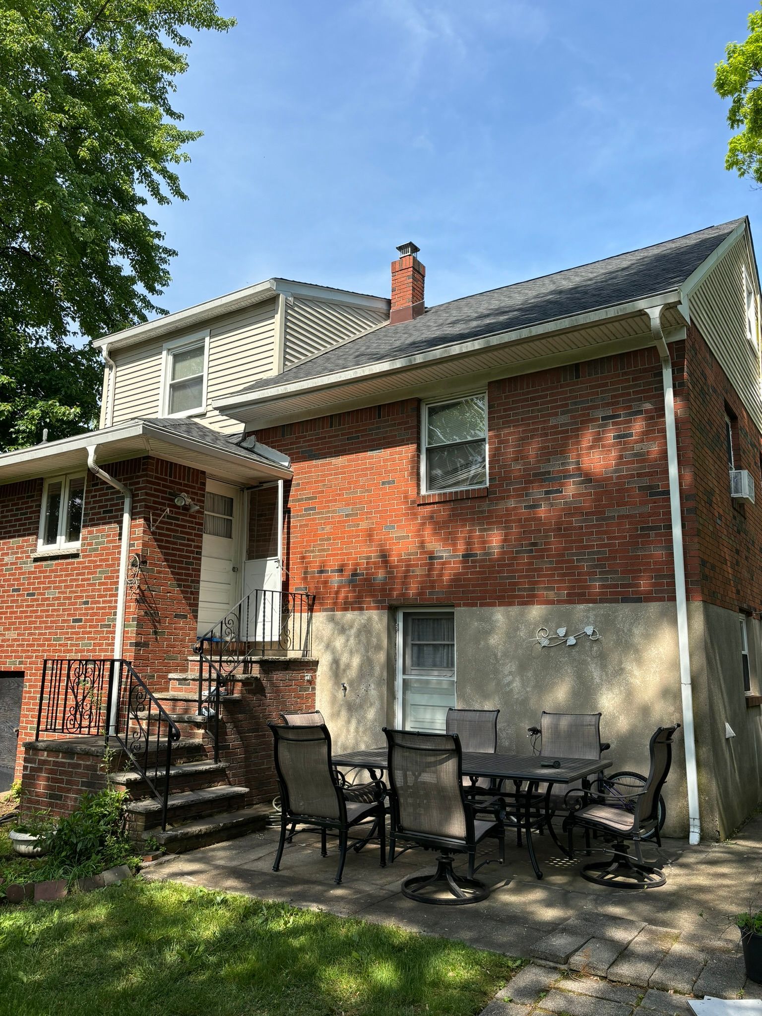 Brick house exterior with patio furniture on a concrete slab, stairs, and a tree.