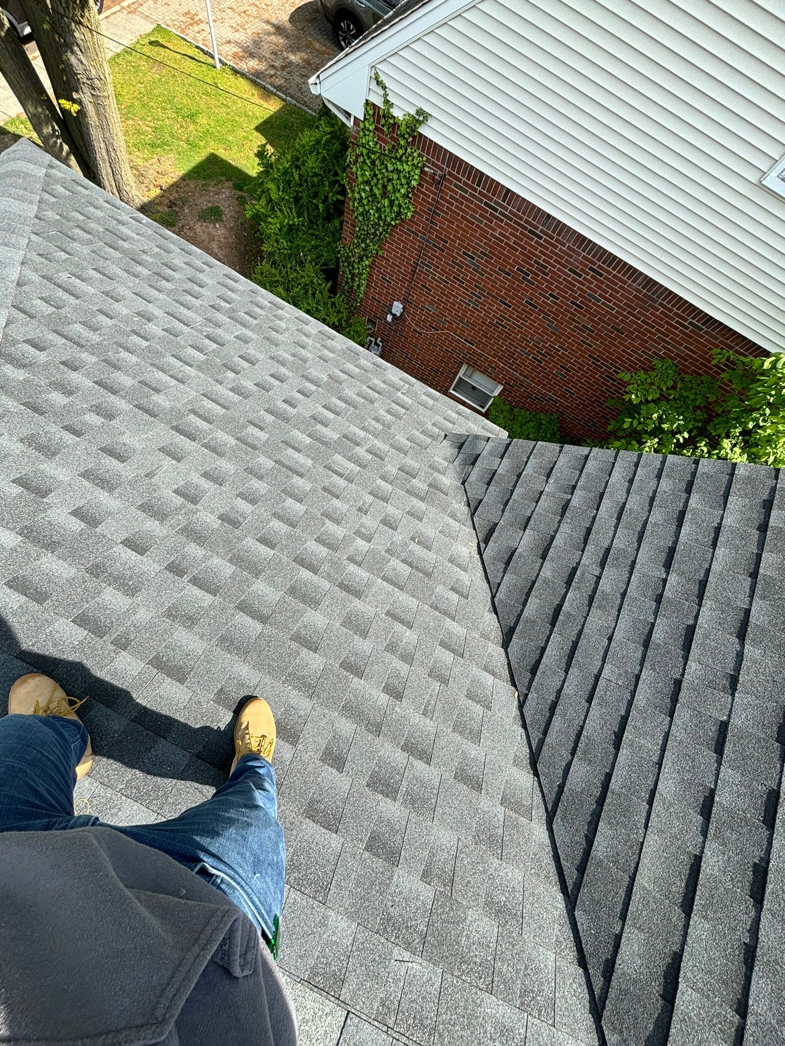 Person on a dark gray shingle roof looking down at a brick building with white siding.