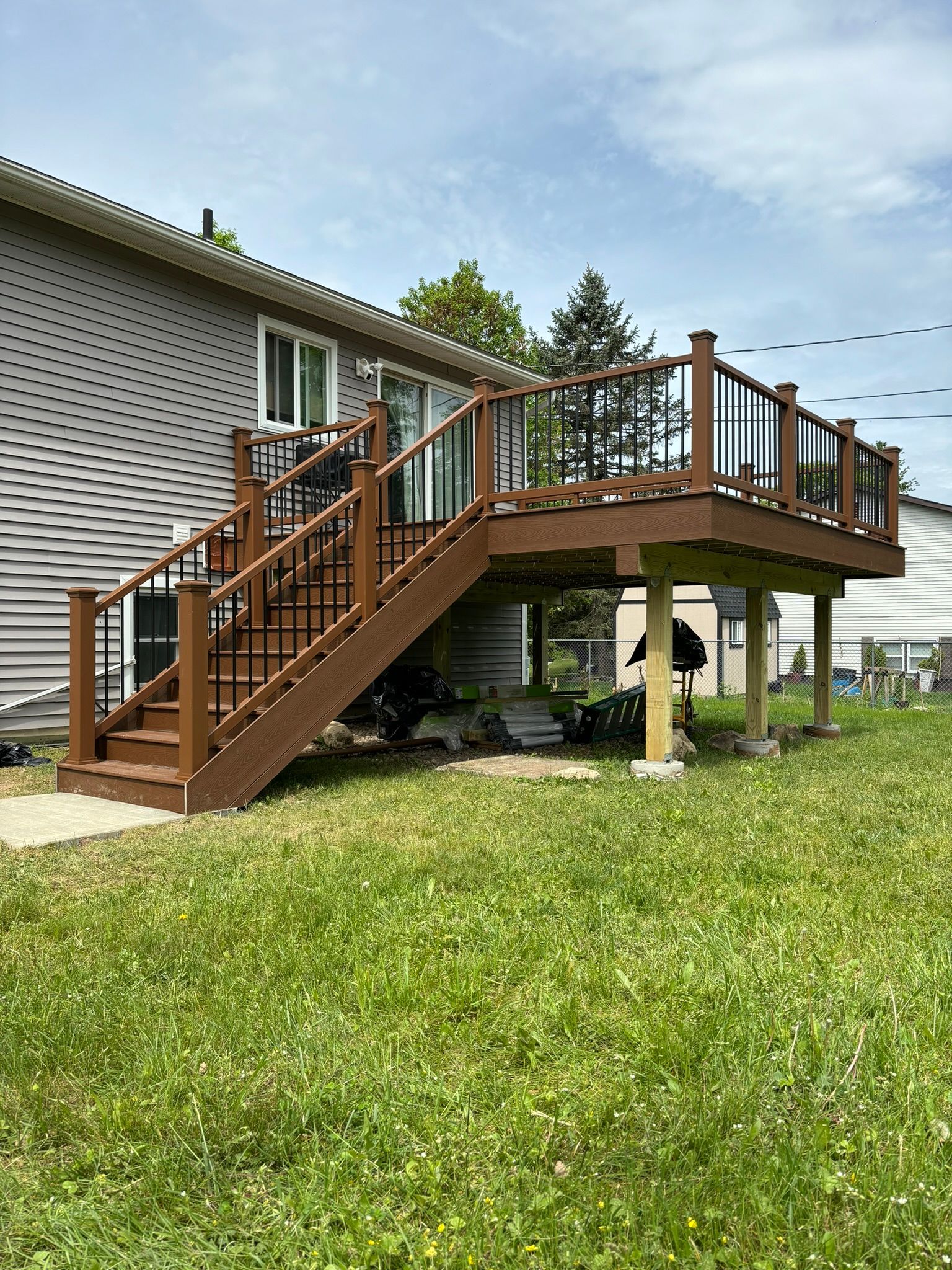 Brown wooden deck with stairs attached to a gray house, set in a grassy yard under a cloudy sky.